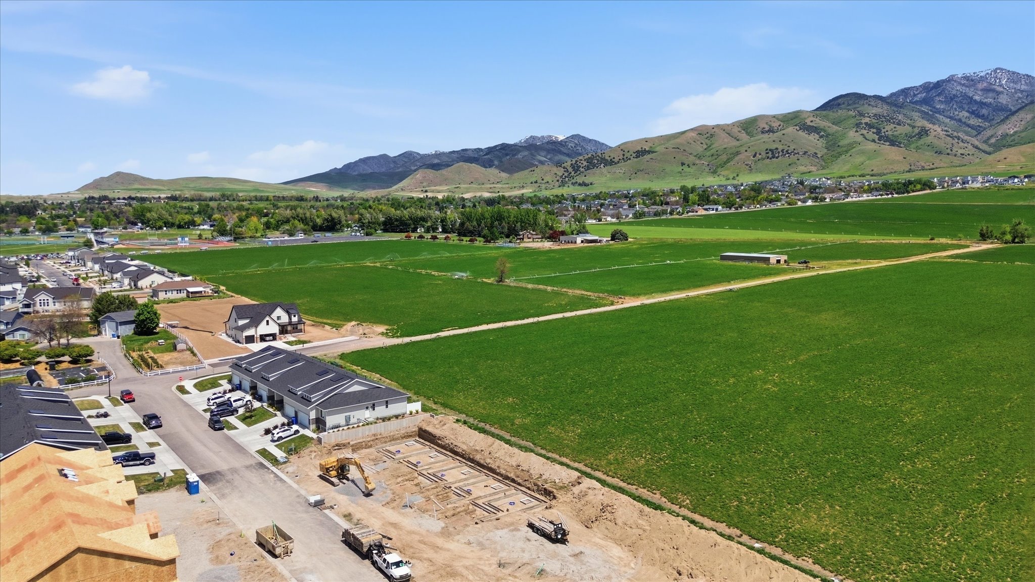 Expansive green fields bordering a developing residential area with distant mountains