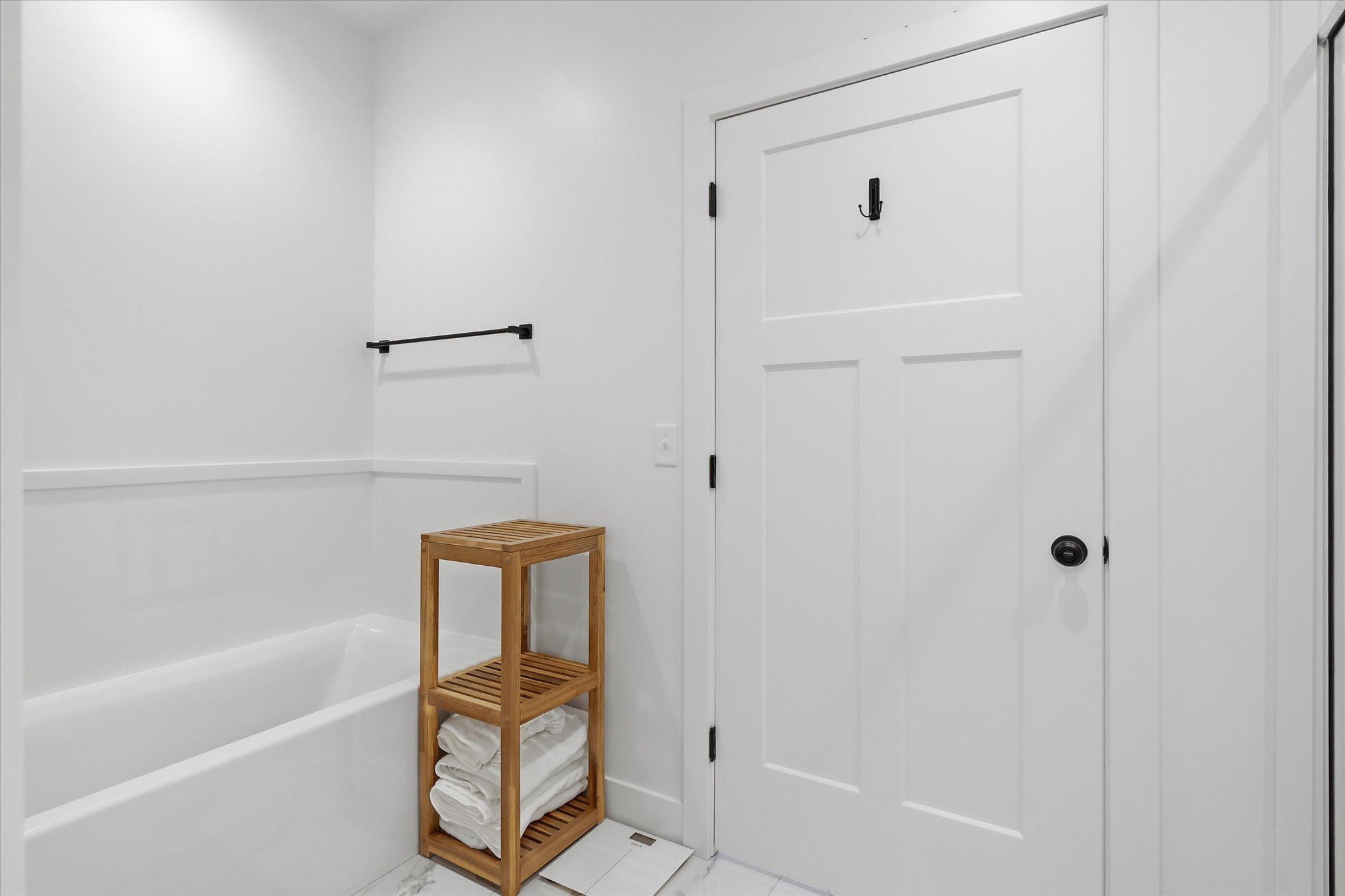 White paneled interior door with matte black hardware, featuring a coordinating matte black towel bar and a white bathtub