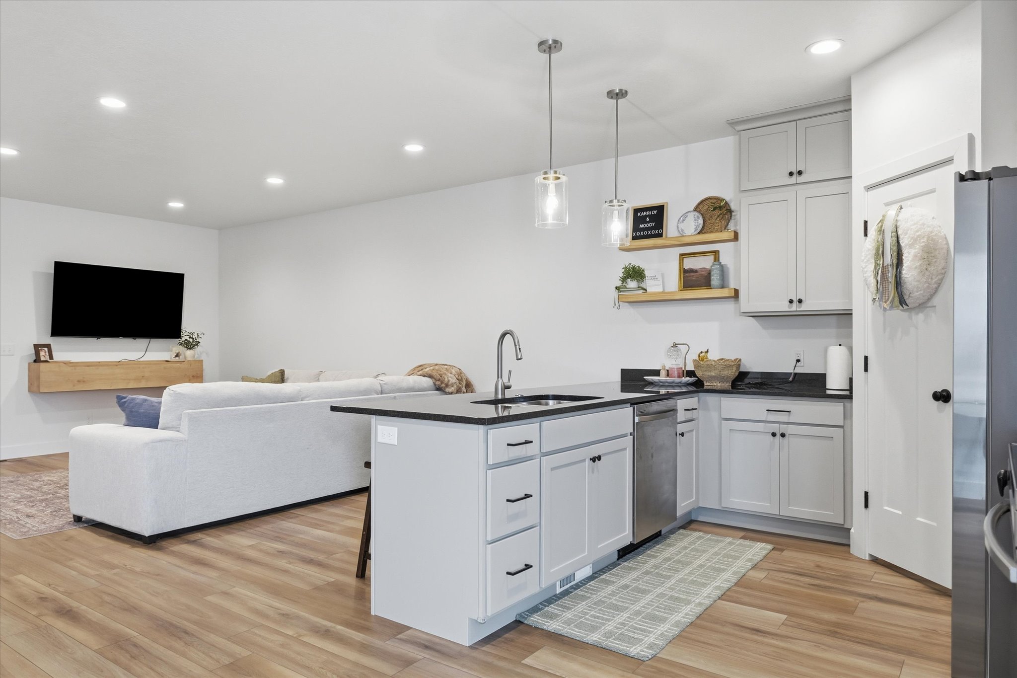 Open-concept kitchen featuring an island with a built-in sink, gray cabinetry, dark countertops, recessed lighting, and wood-finish flooring