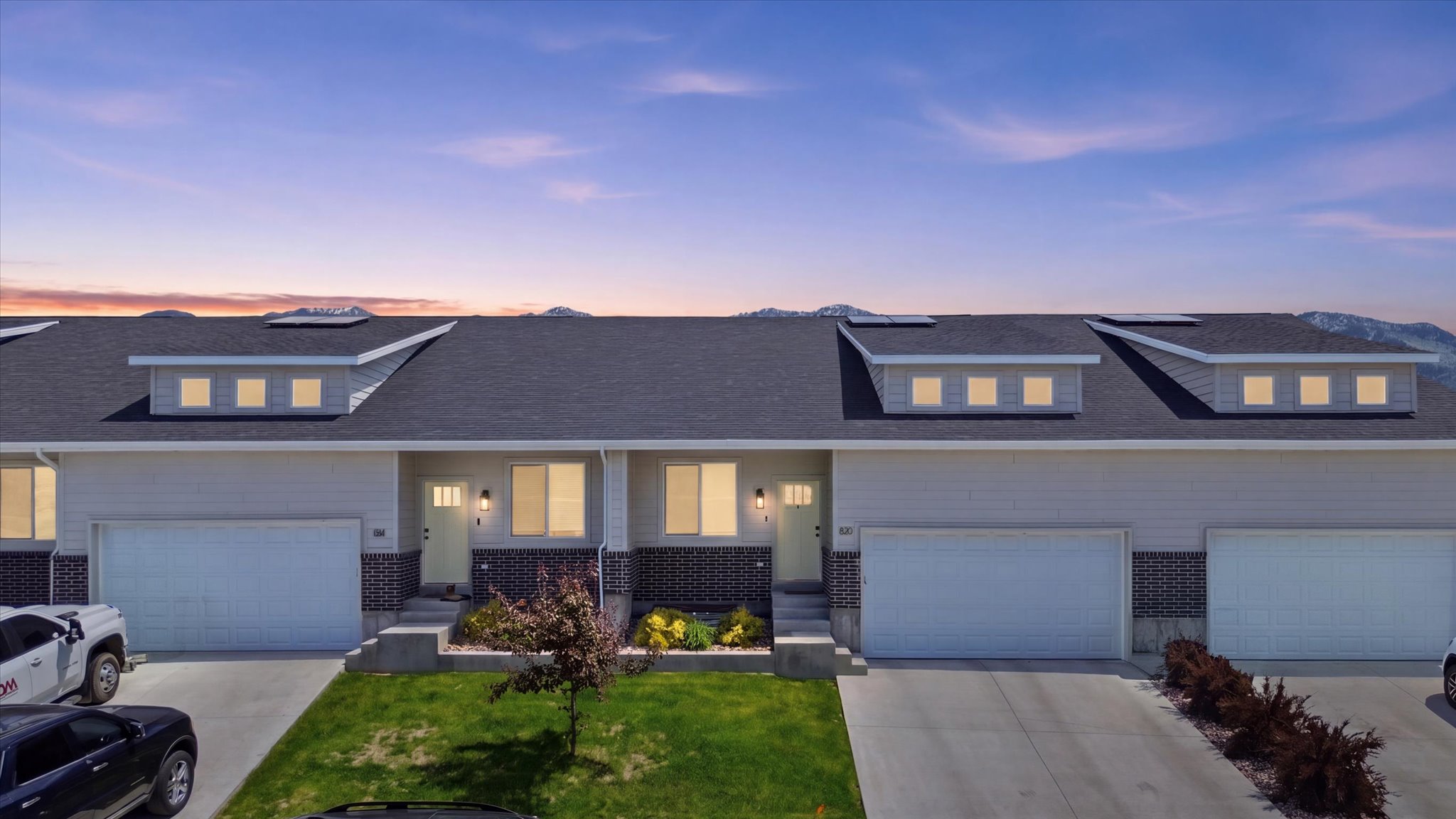 Multi-unit property featuring dormer windows, attached garages, and a paved driveway