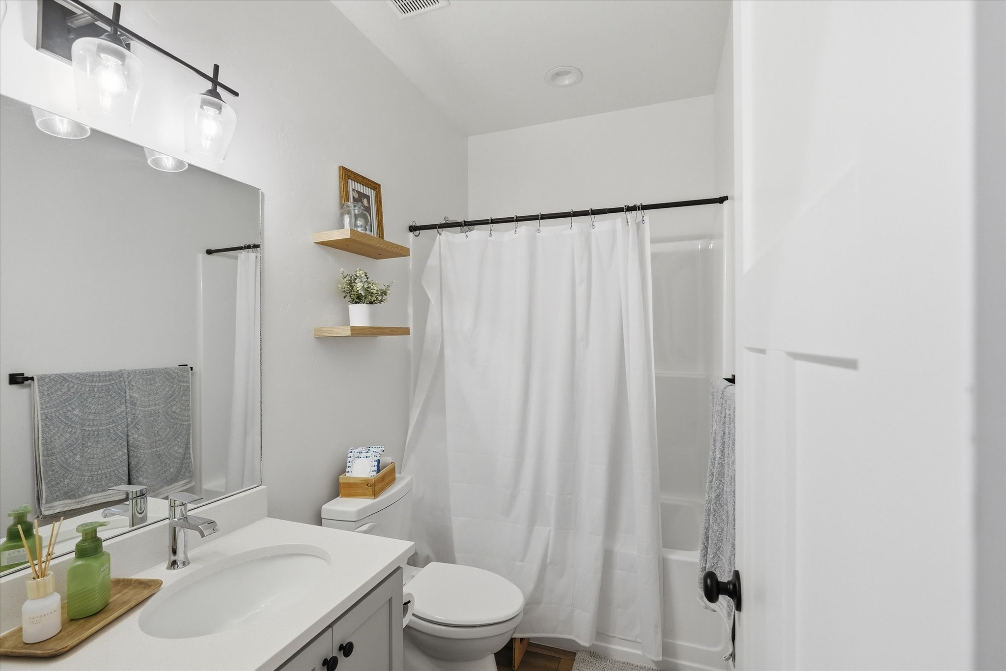 Bathroom featuring a single vanity with a white countertop and undermount sink, a large mirror, and a shower-tub combination
