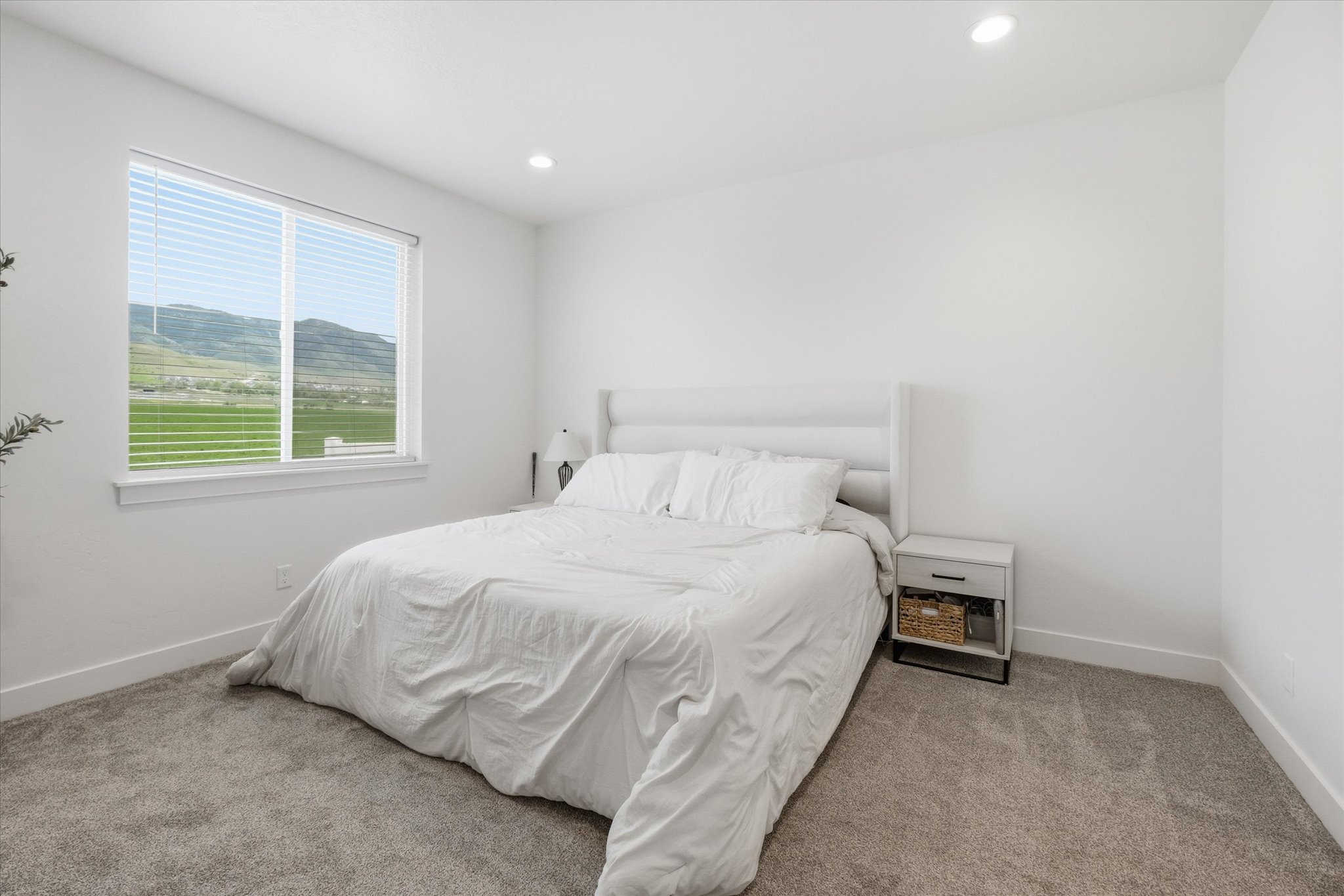 Bedroom featuring a large window with horizontal blinds, showcasing distant green hills