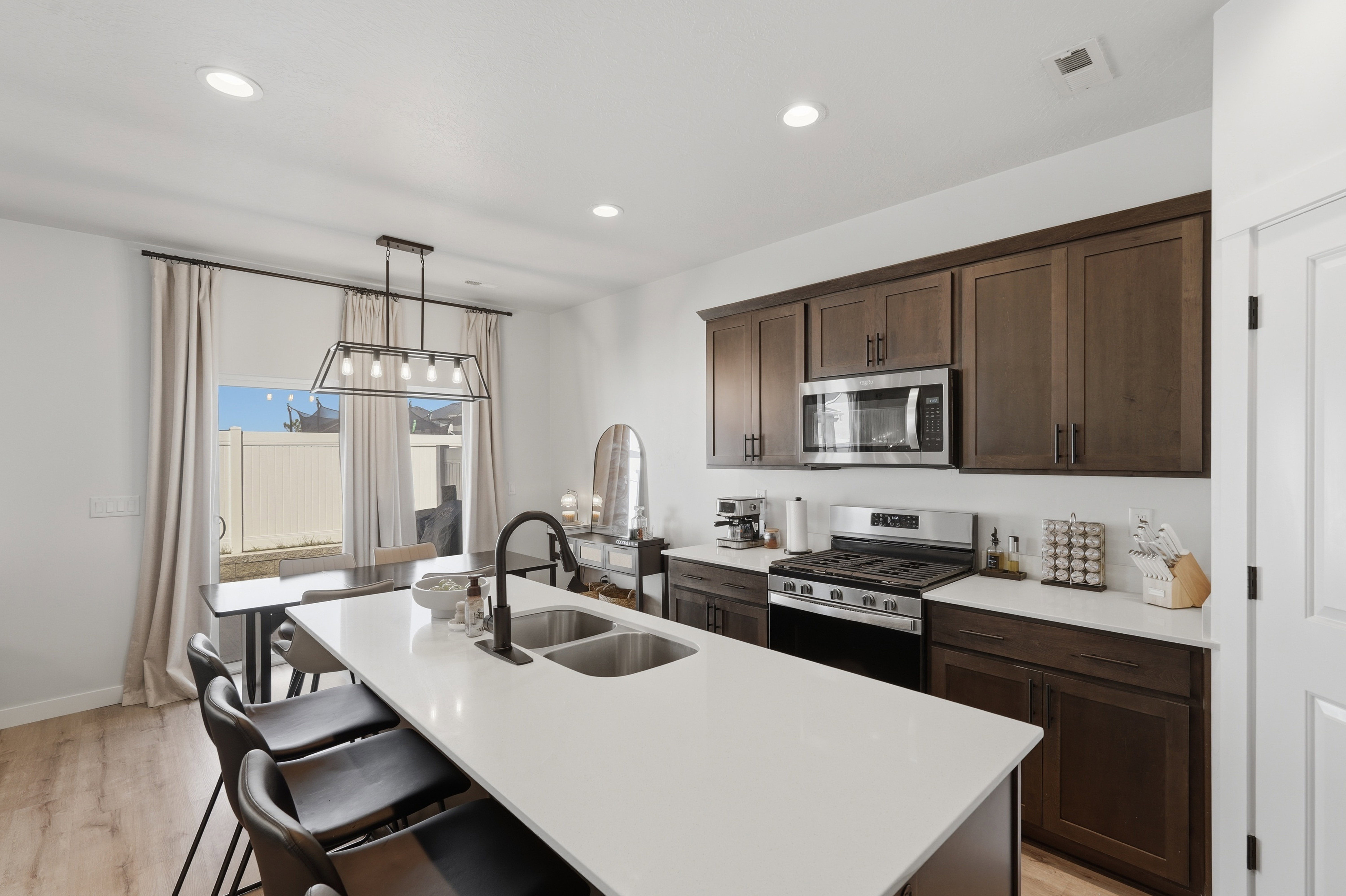 Bright kitchen featuring a central island with a double basin sink, dark wood-finish cabinetry, stainless steel appliances, a gas range, and wood-finish flooring