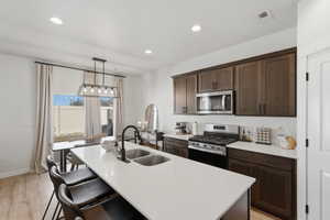 Bright kitchen featuring a central island with a double basin sink, dark wood-finish cabinetry, stainless steel appliances, a gas range, and wood-finish flooring