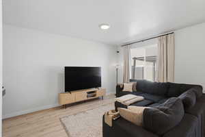 Bright interior space featuring light-colored walls, wood-finish flooring, and a large window with privacy blinds