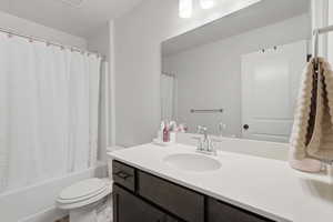 Bathroom featuring a white bathtub and toilet, a dark wood-finish vanity with a white countertop, a chrome faucet, and a large wall-mounted mirror