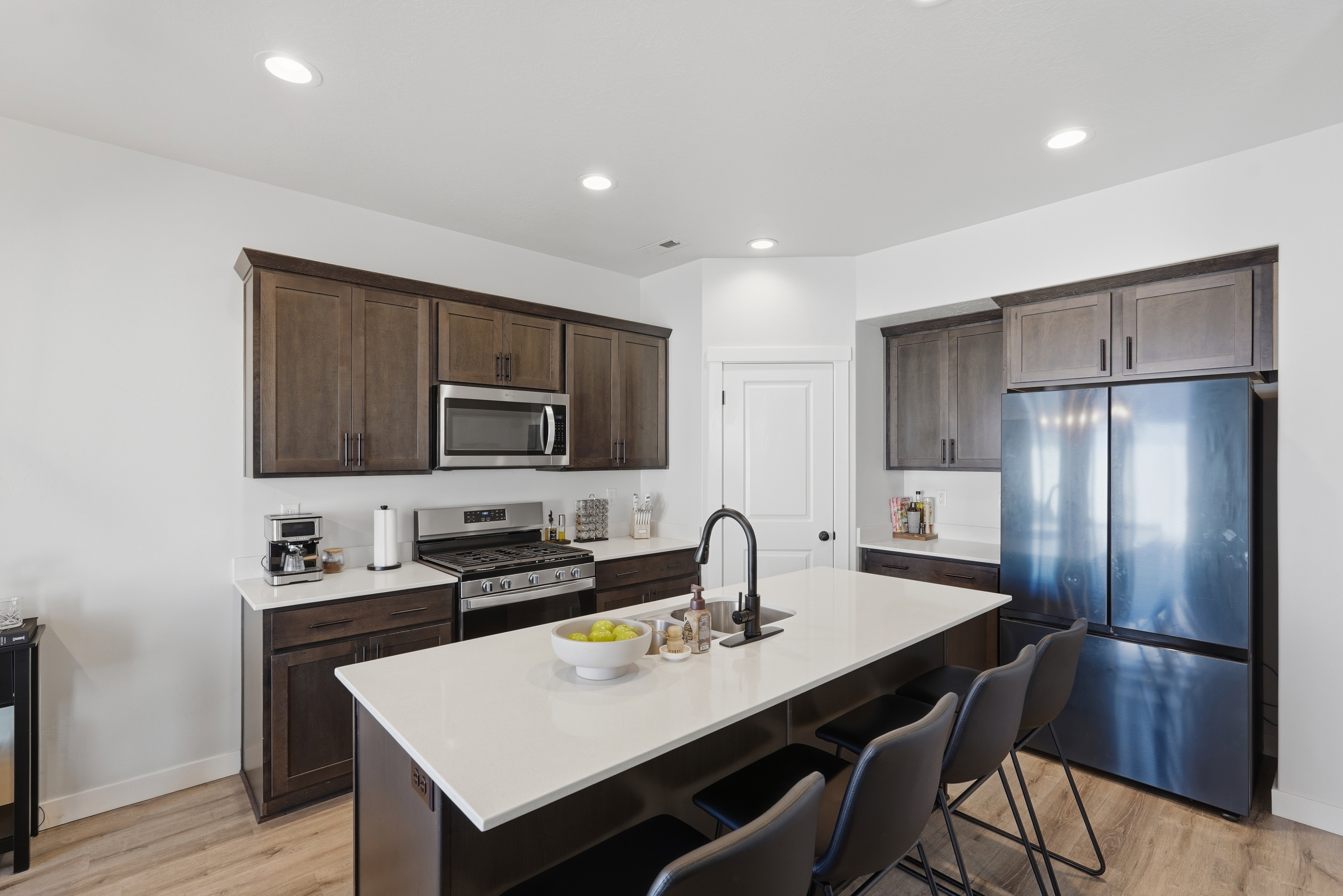 Kitchen featuring an expansive island with a matte black faucet, dark wood-finish cabinetry, stainless steel appliances, and white countertops
