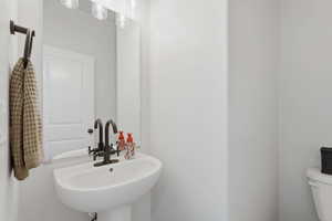Pedestal sink featuring a contemporary bronze-finish faucet, rectangular wall mirror, and a three-light vanity fixture
