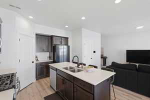 Kitchen featuring a central island with dual sinks, light-toned countertops, dark wood-finish cabinetry, stainless steel appliances, and wood-finish flooring