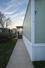 Property exterior featuring light green siding and white trim, with a concrete pathway leading to a covered entry with wood stairs