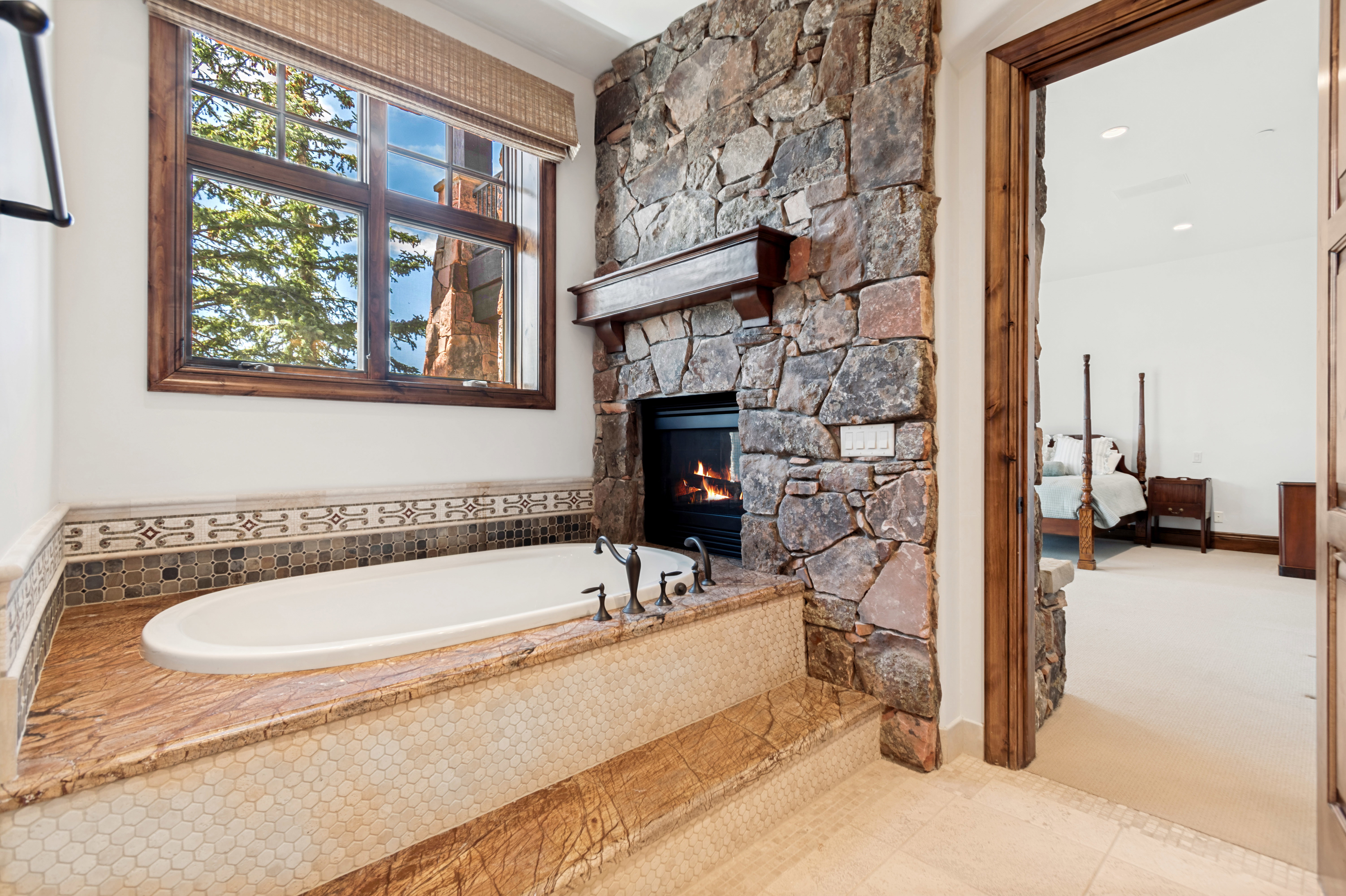 Soaking tub with a stone surround, integrated fireplace, and wood-framed window