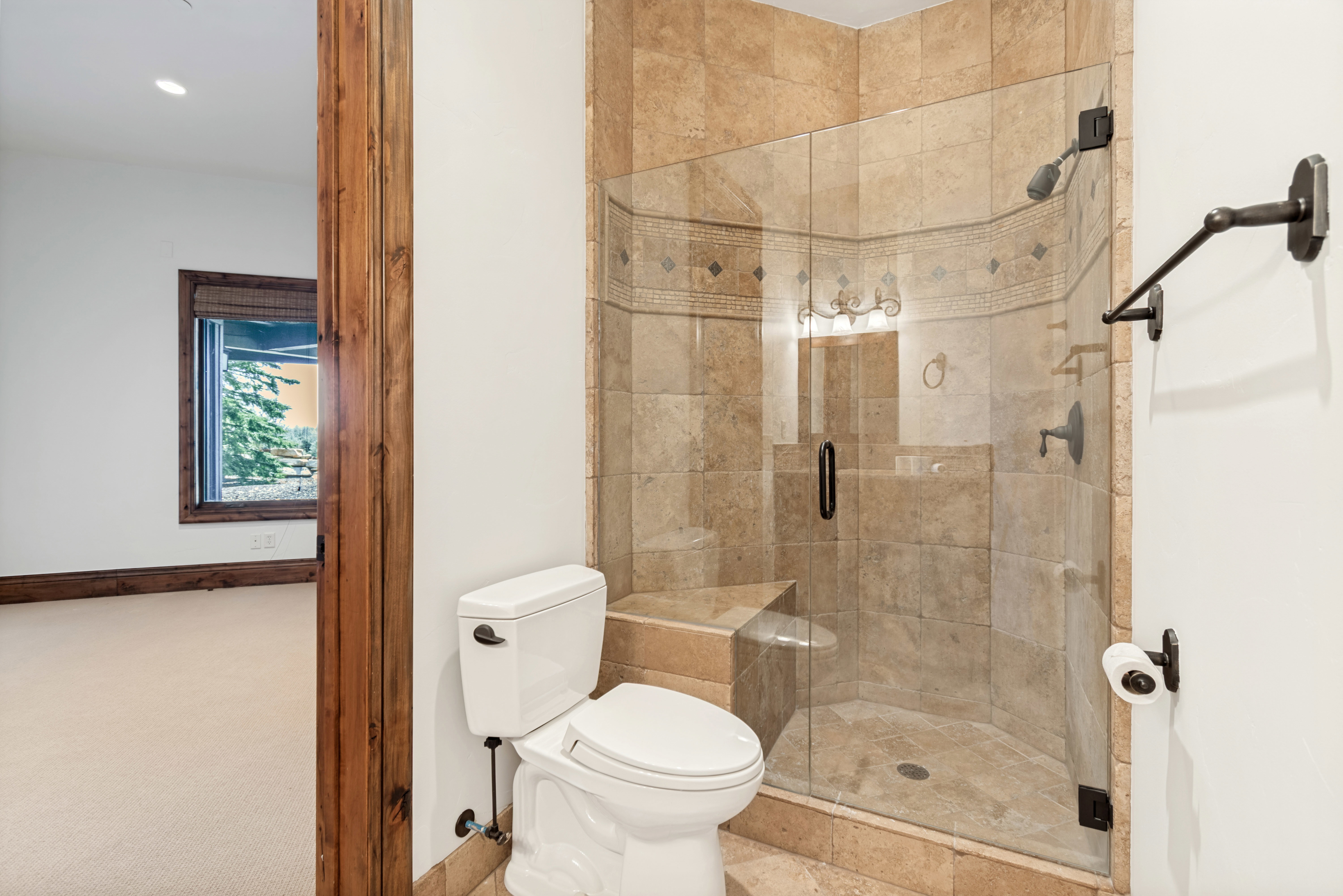 Glass-enclosed shower featuring natural stone tile, an integrated shower bench, and dark bronze fixtures