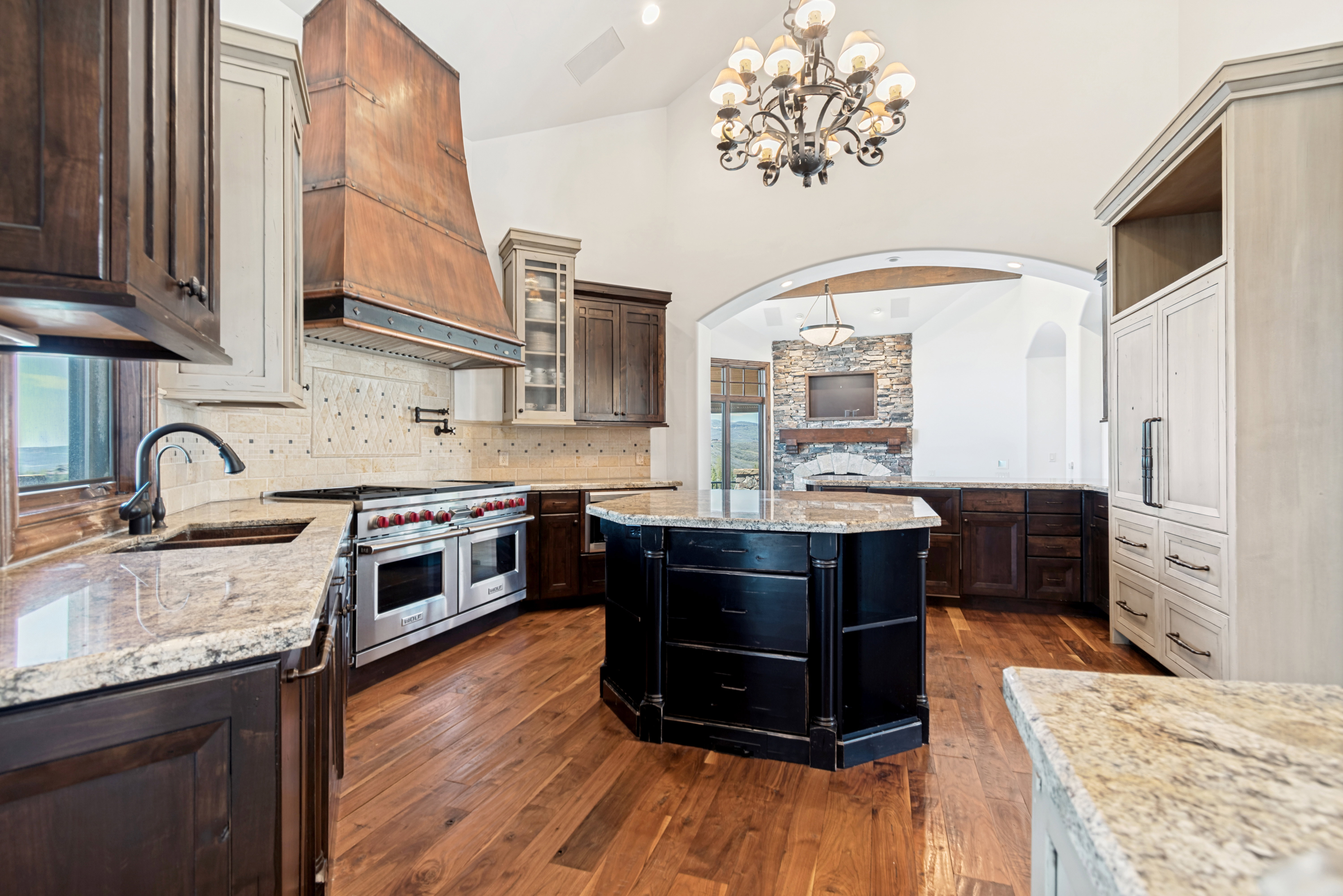 Gourmet kitchen featuring a large professional-grade range, custom copper range hood, wood-finish flooring, granite countertops, and a central island with integrated storage