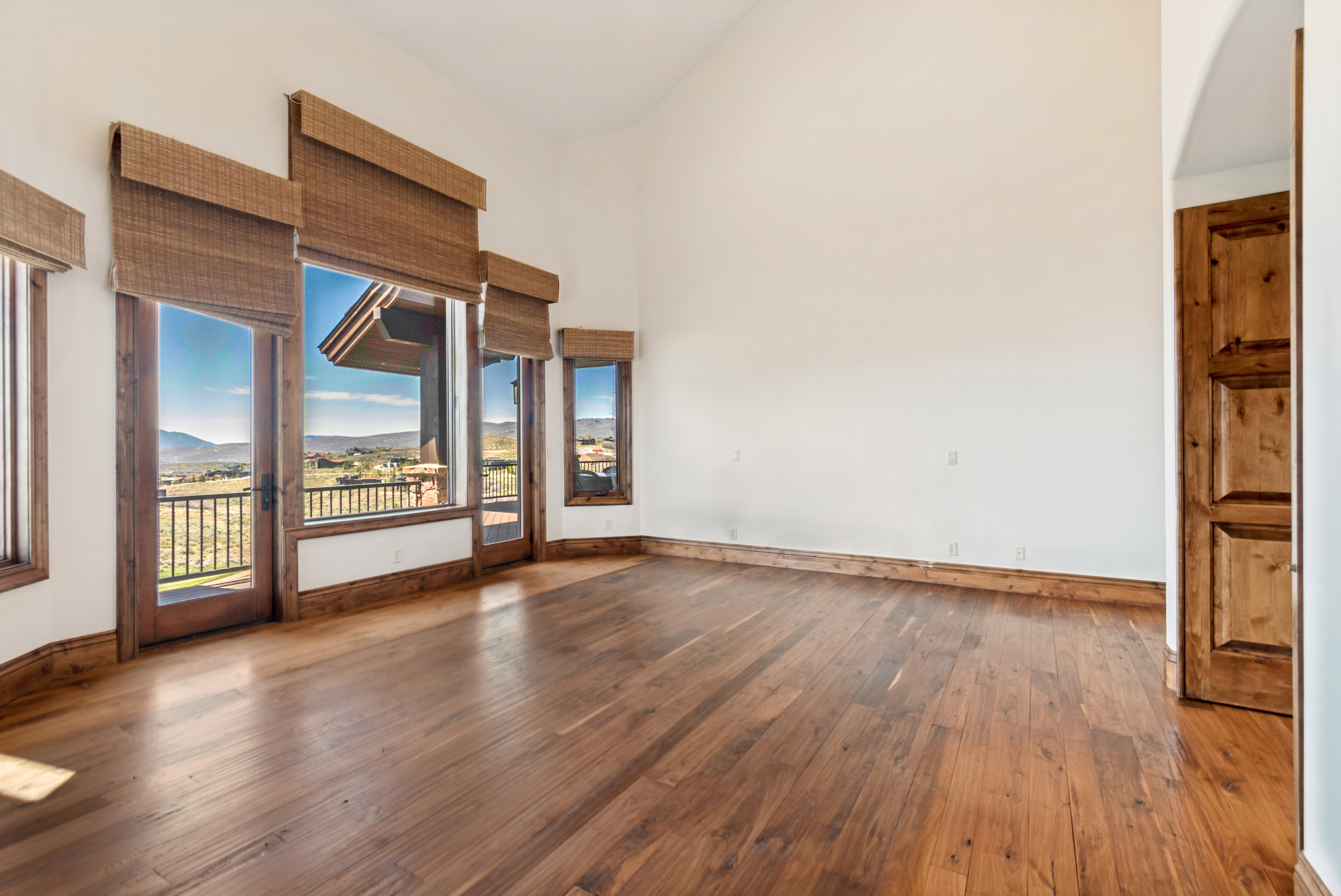 Spacious room featuring wood-finish flooring, high ceilings, multiple wood-framed windows, and French doors leading to an exterior balcony