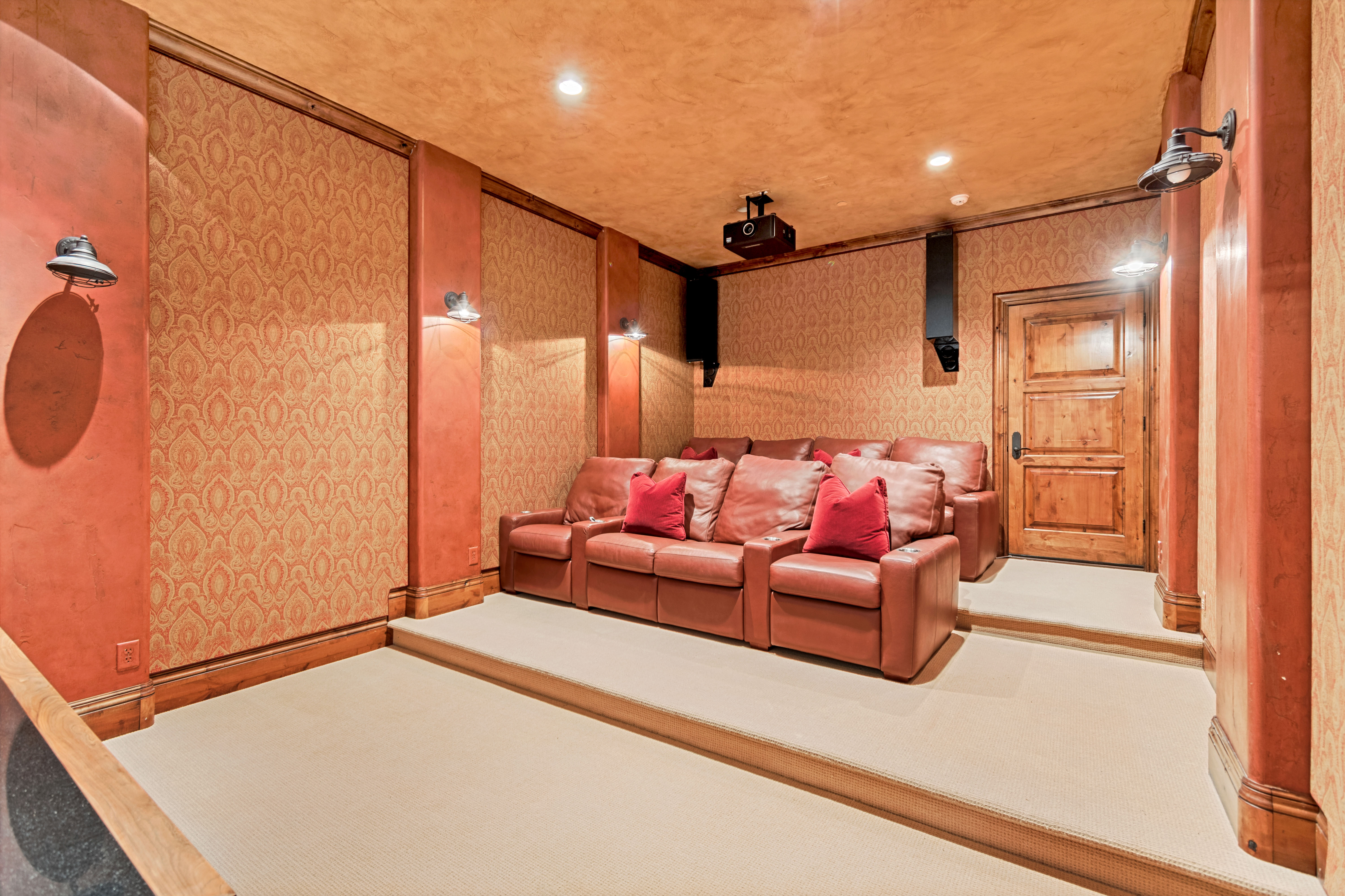 Dedicated media room featuring tiered seating, patterned wall coverings, wood trim, recessed lighting, and a ceiling-mounted projector