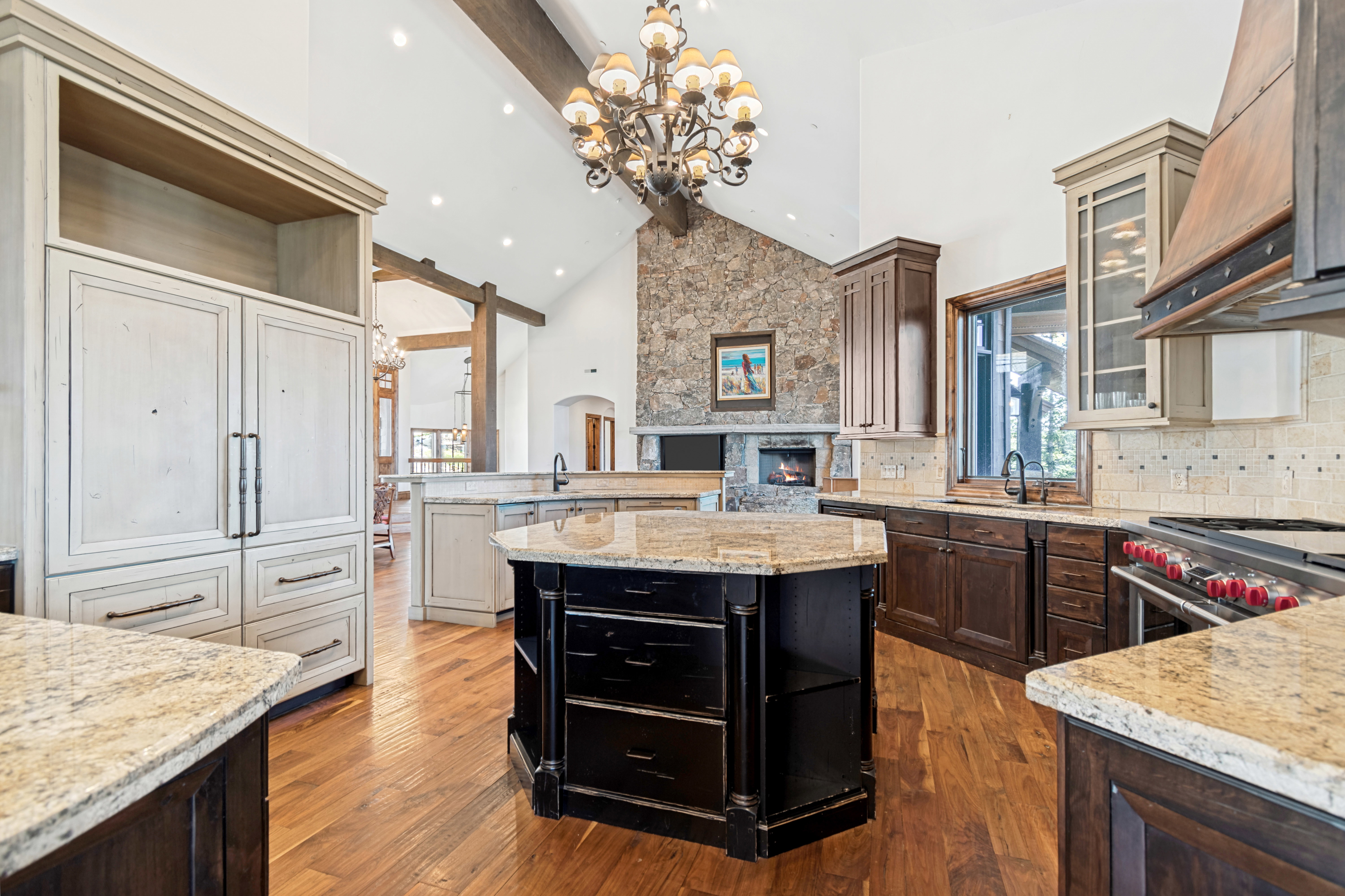 Spacious kitchen featuring varied cabinetry finishes, multiple granite-topped islands, and a stone accent wall with an integrated fireplace