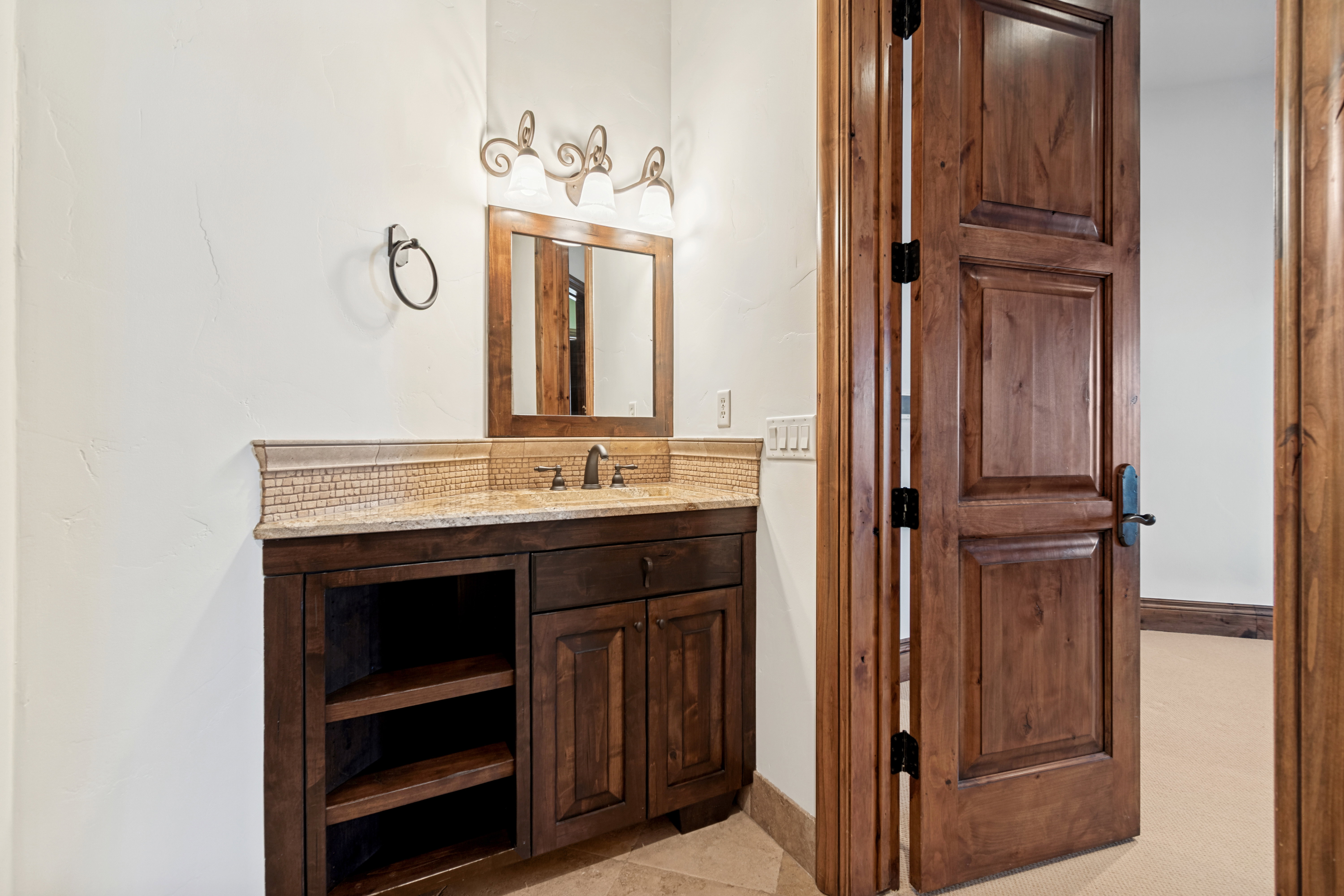 Powder room featuring a wood-finish vanity with built-in shelving, stone-finish countertop, and decorative tile backsplash
