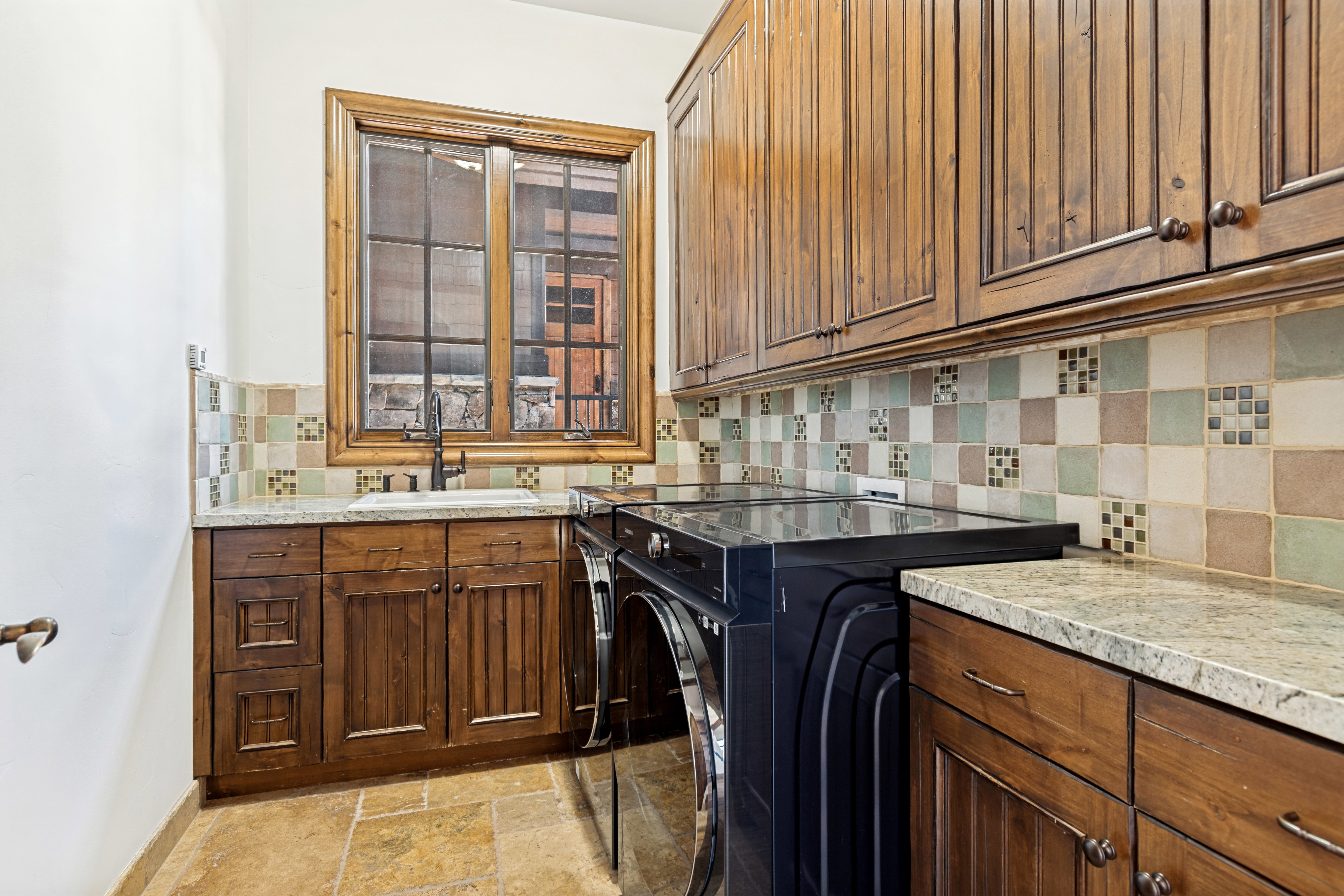 Utility area featuring wood-finish cabinetry, granite-style countertops, and a decorative tile backsplash