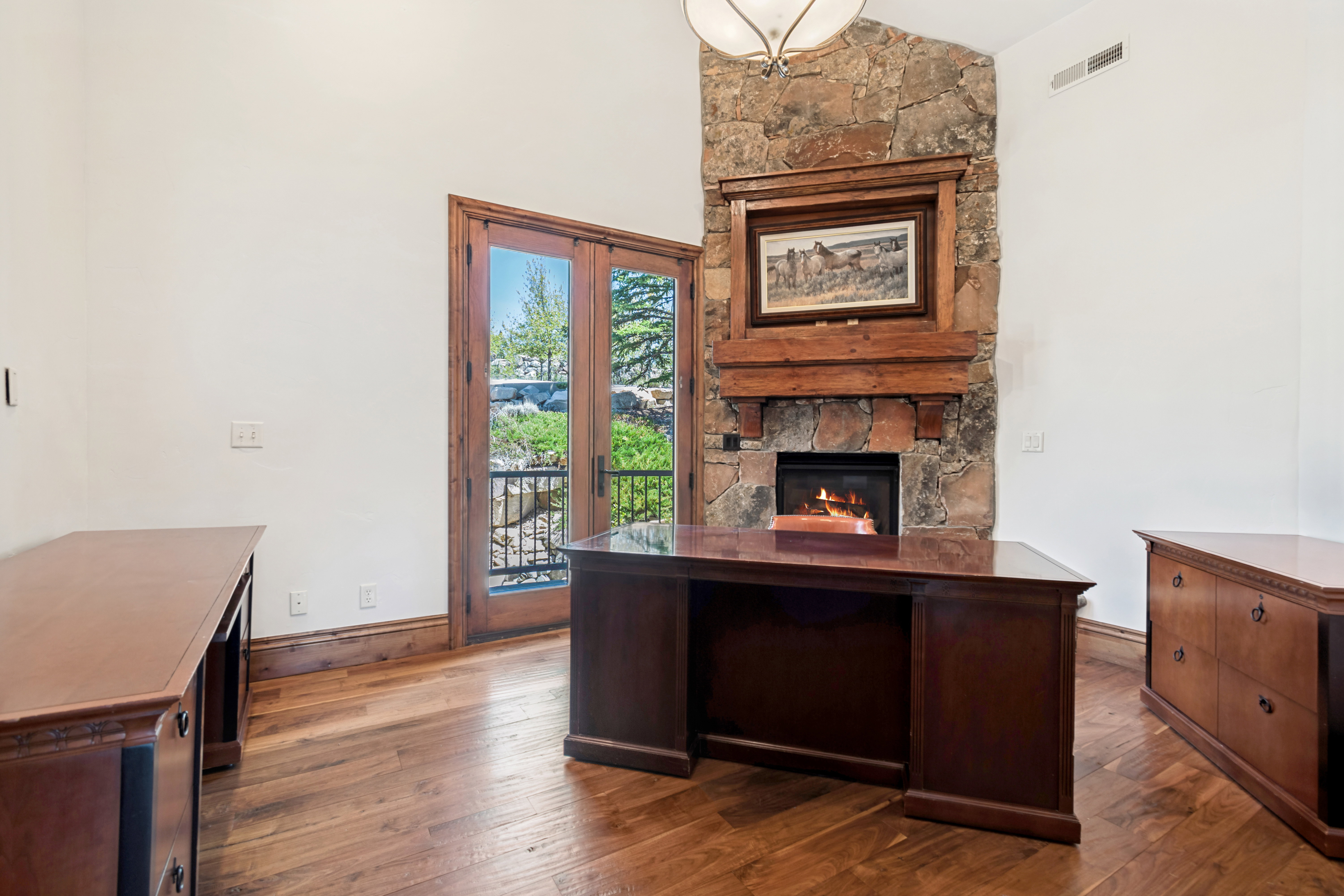 Interior space featuring a stone fireplace with a wood mantle, wood-finish flooring, and French doors opening to a balcony with metal railings