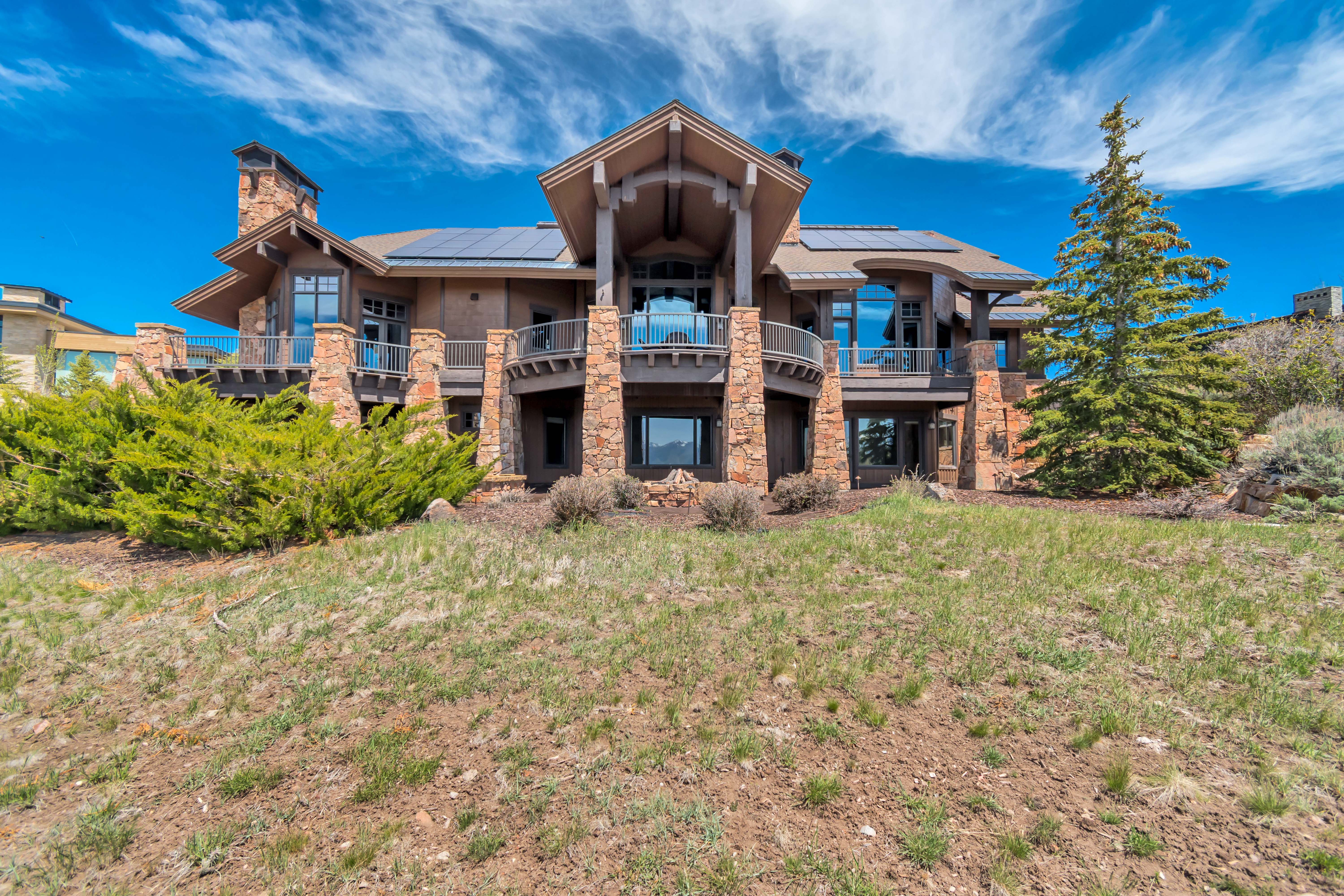 Multi-level residence featuring stone and stucco exterior, prominent stone chimney, multiple balconies with metal railings, and integrated solar panels