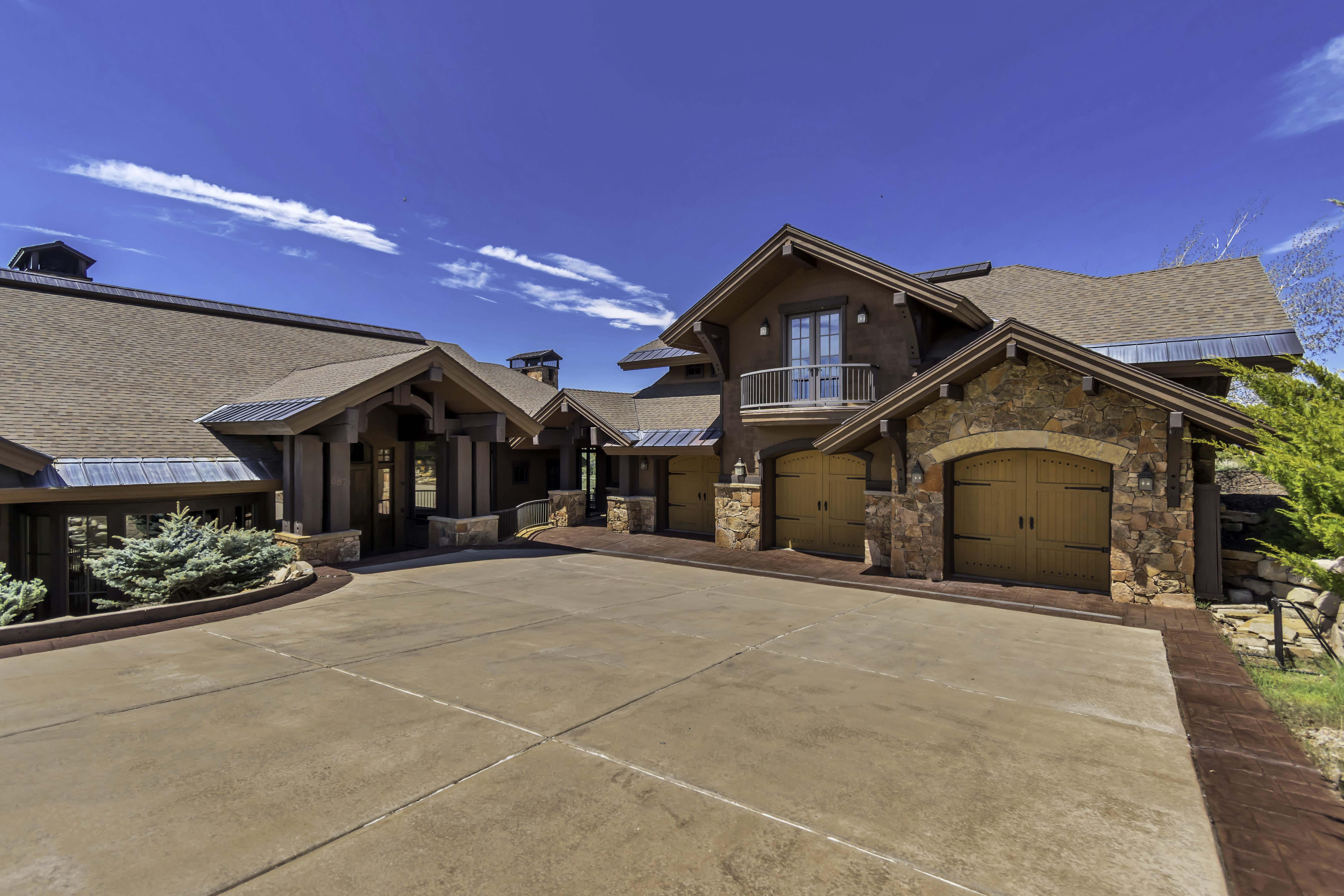 Expansive concrete driveway with a stamped concrete border, multi-car garage with arched wooden doors, and exterior stone accents