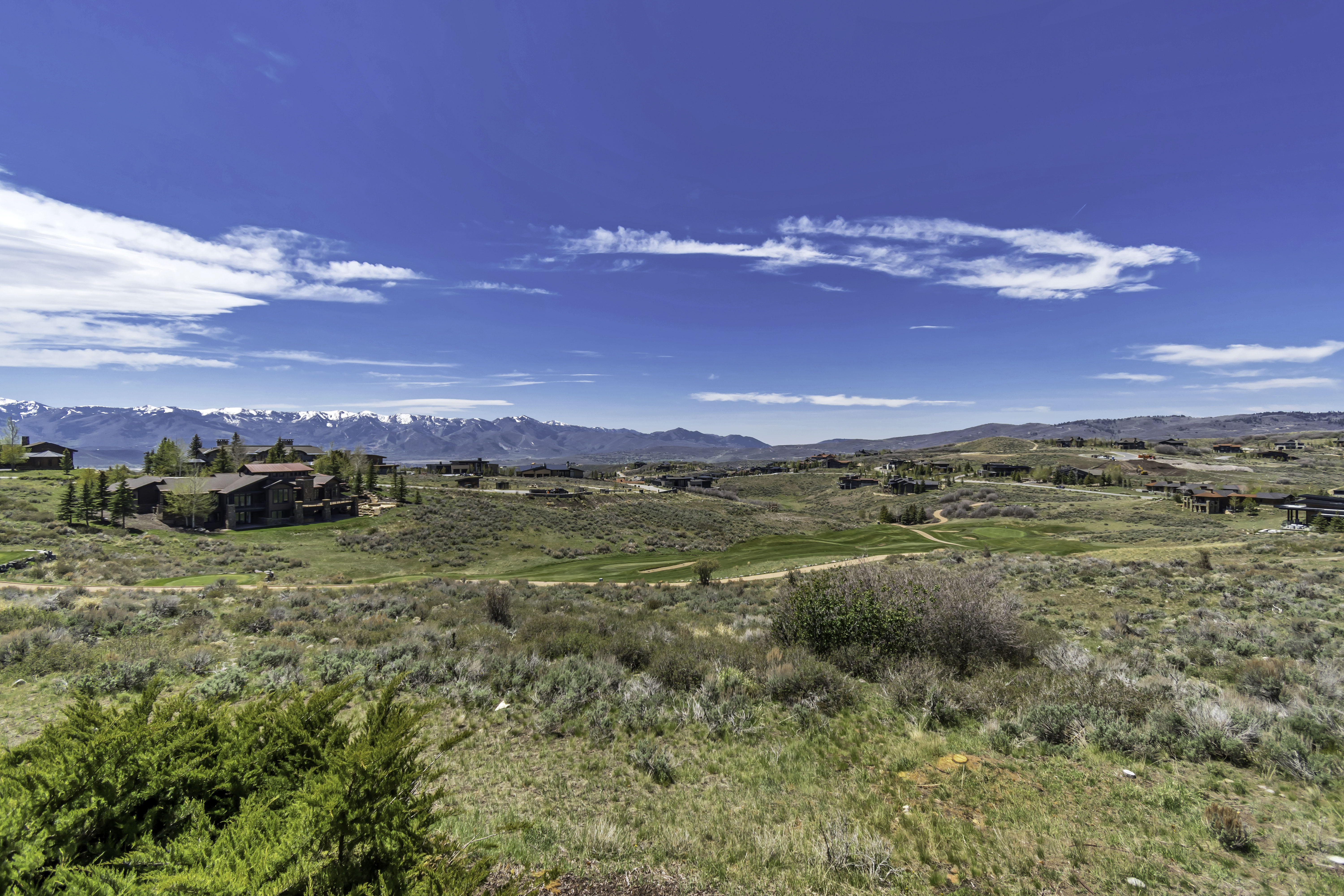 Expansive high-desert landscape featuring distant snow-capped mountains, a golf course, and multiple residential properties under a clear blue sky