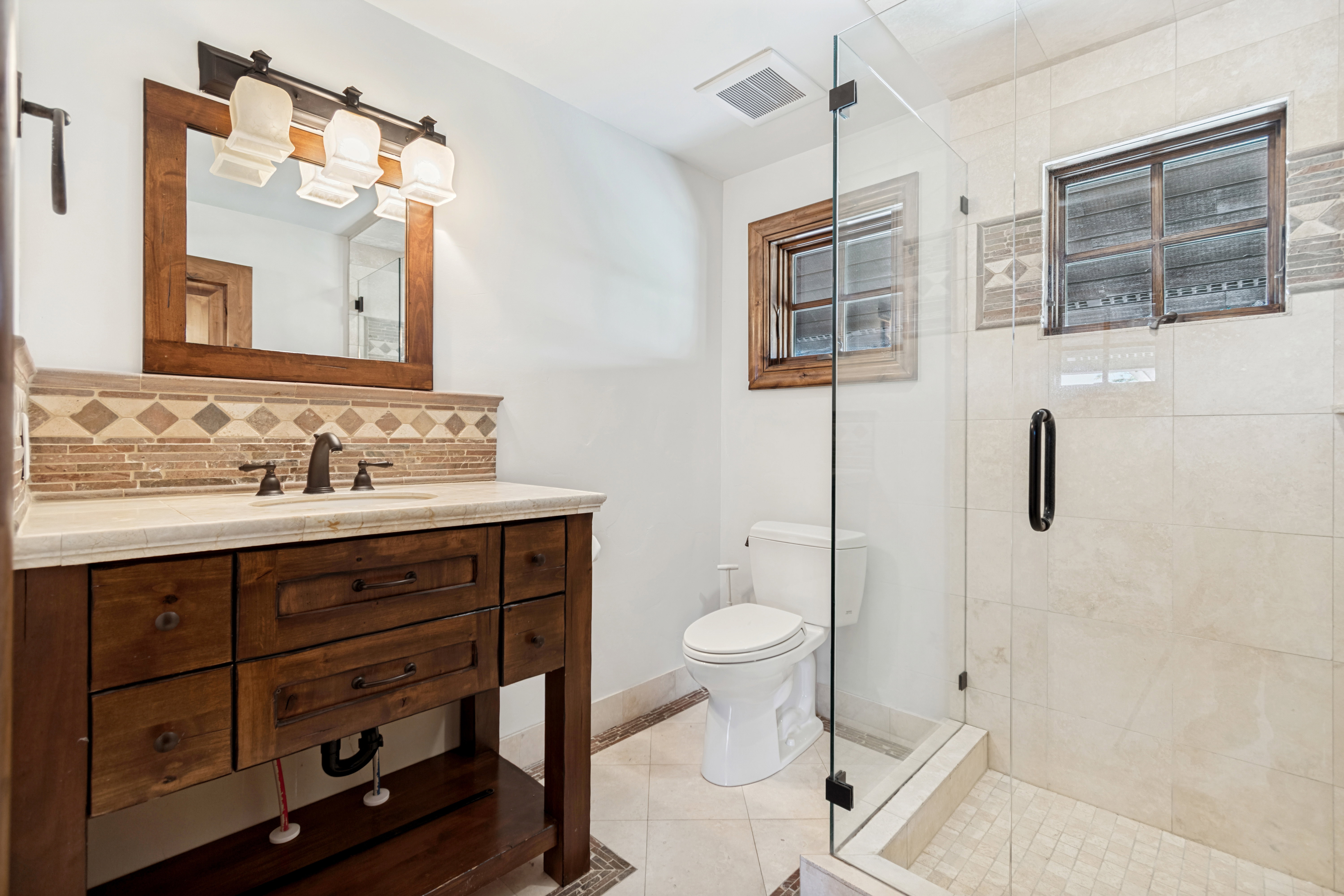 Bathroom featuring a dark wood vanity with a light-colored countertop, mosaic tile backsplash, and an overhead light fixture with three sconces