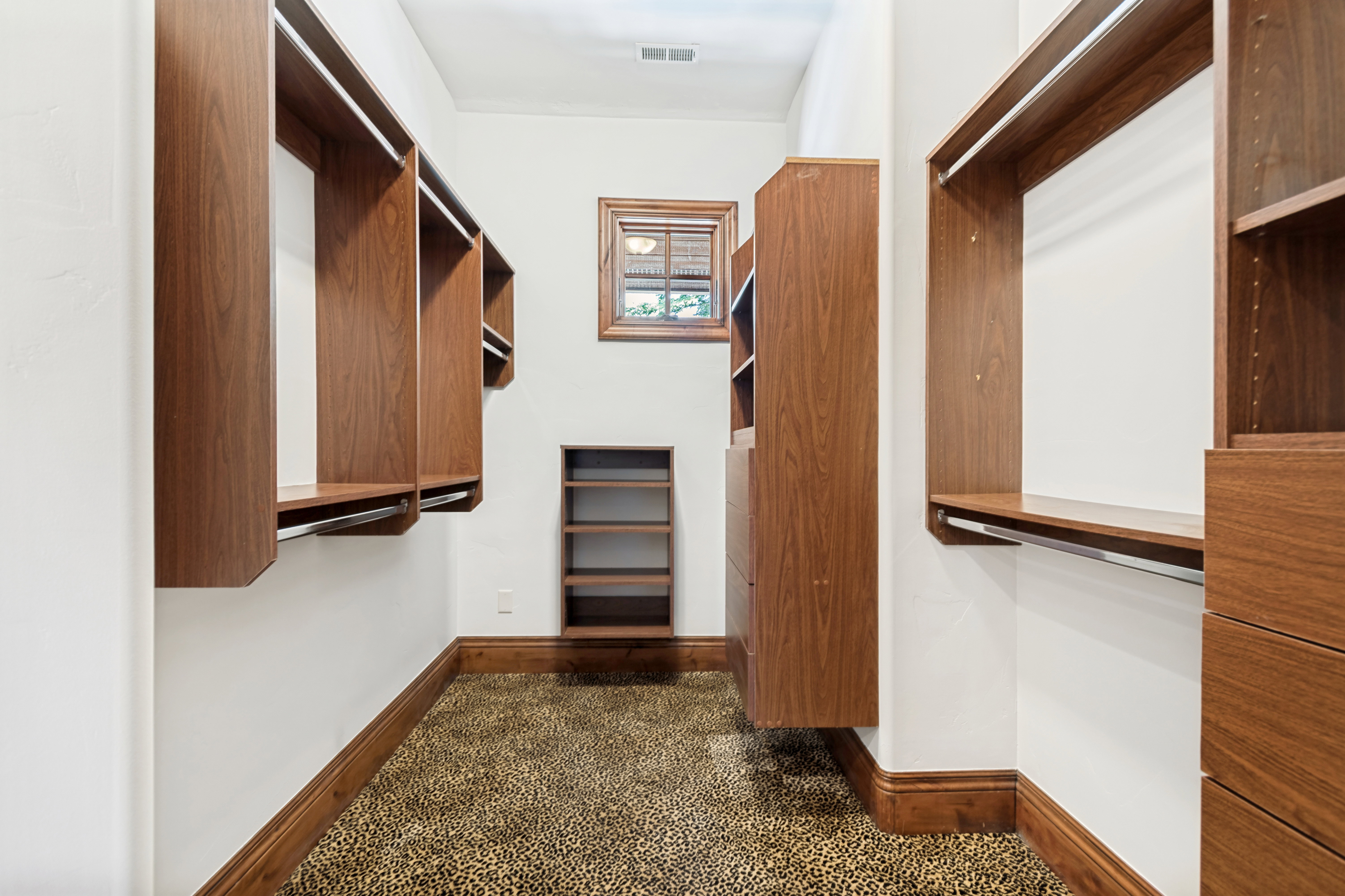 Walk-in closet featuring extensive built-in wood-finish shelving and hanging rods