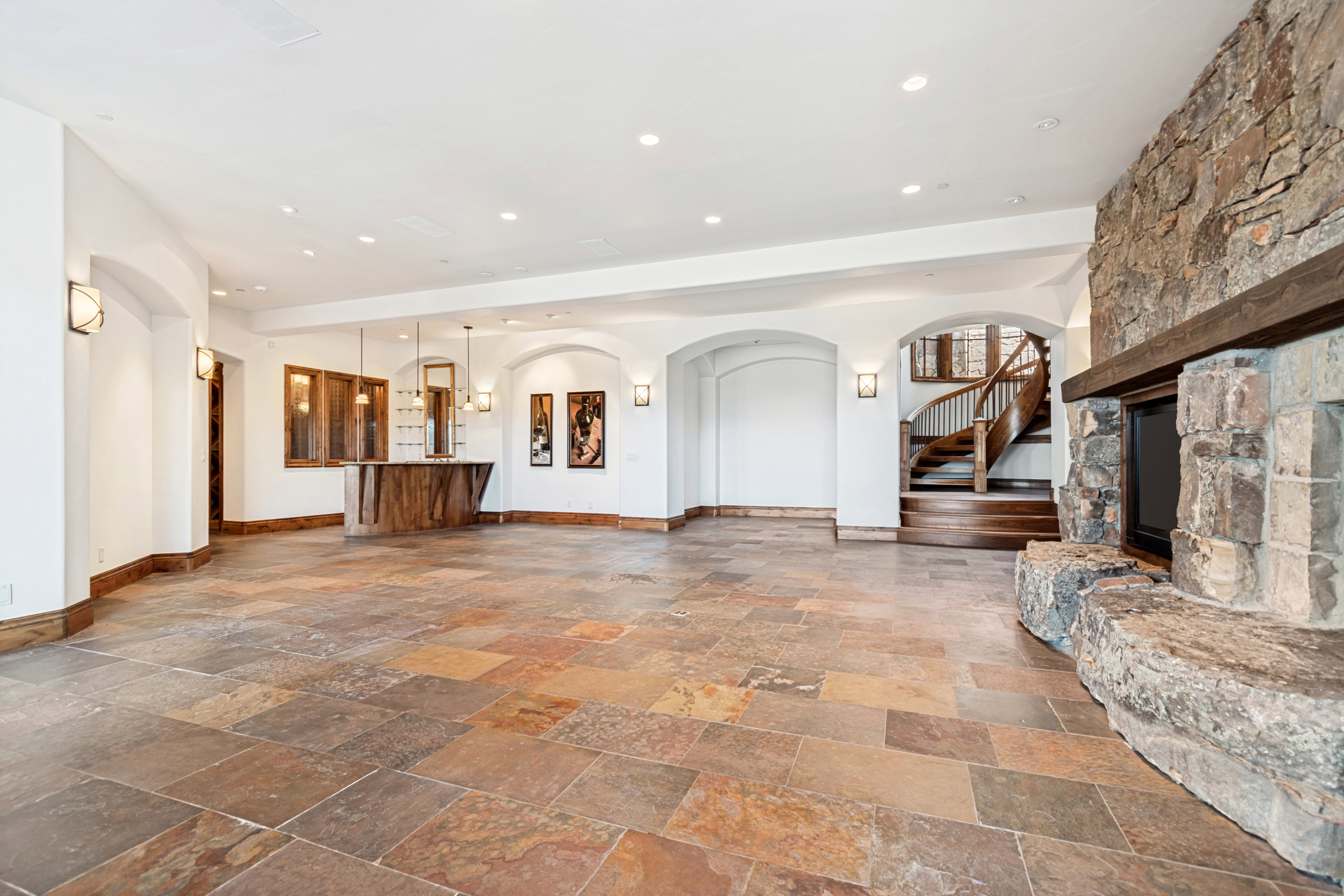 Spacious room featuring multi-toned stone flooring, a stone fireplace with a substantial hearth, and a custom wood bar area with built-in cabinetry