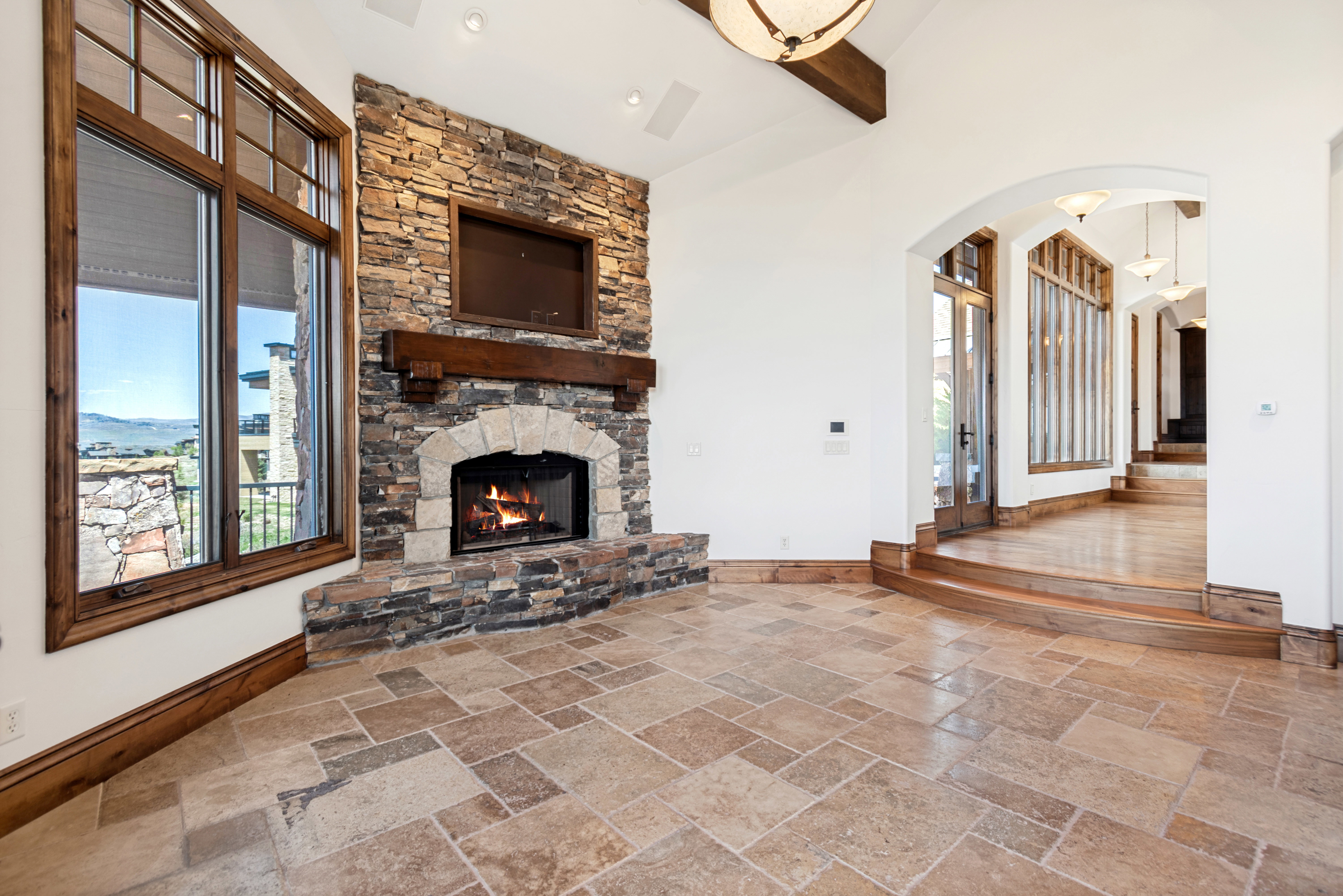 Stone fireplace with a substantial timber mantel and hearth, set against large wood-framed windows