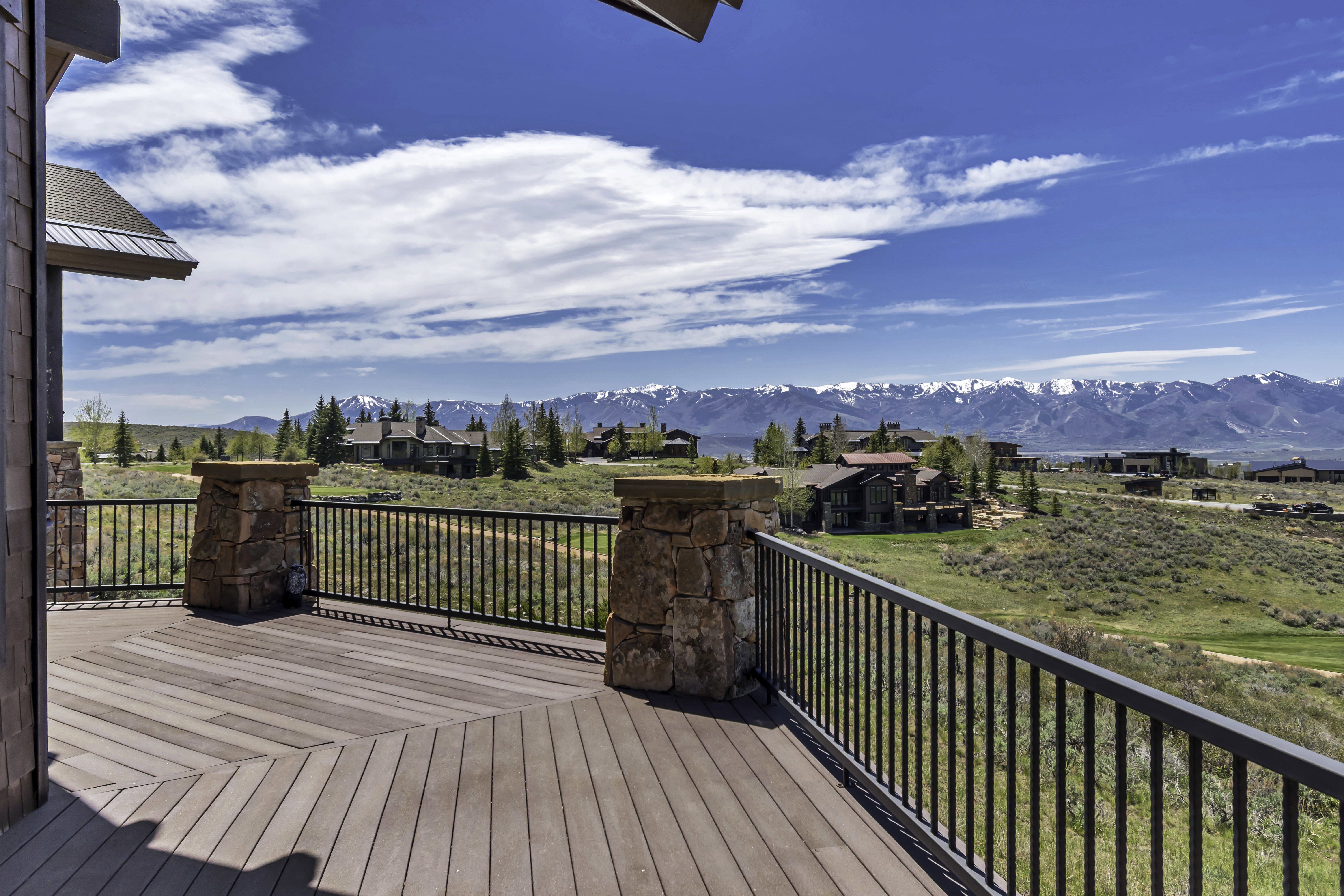 Outdoor deck featuring wood-finish flooring, stone pillars, and a metal railing