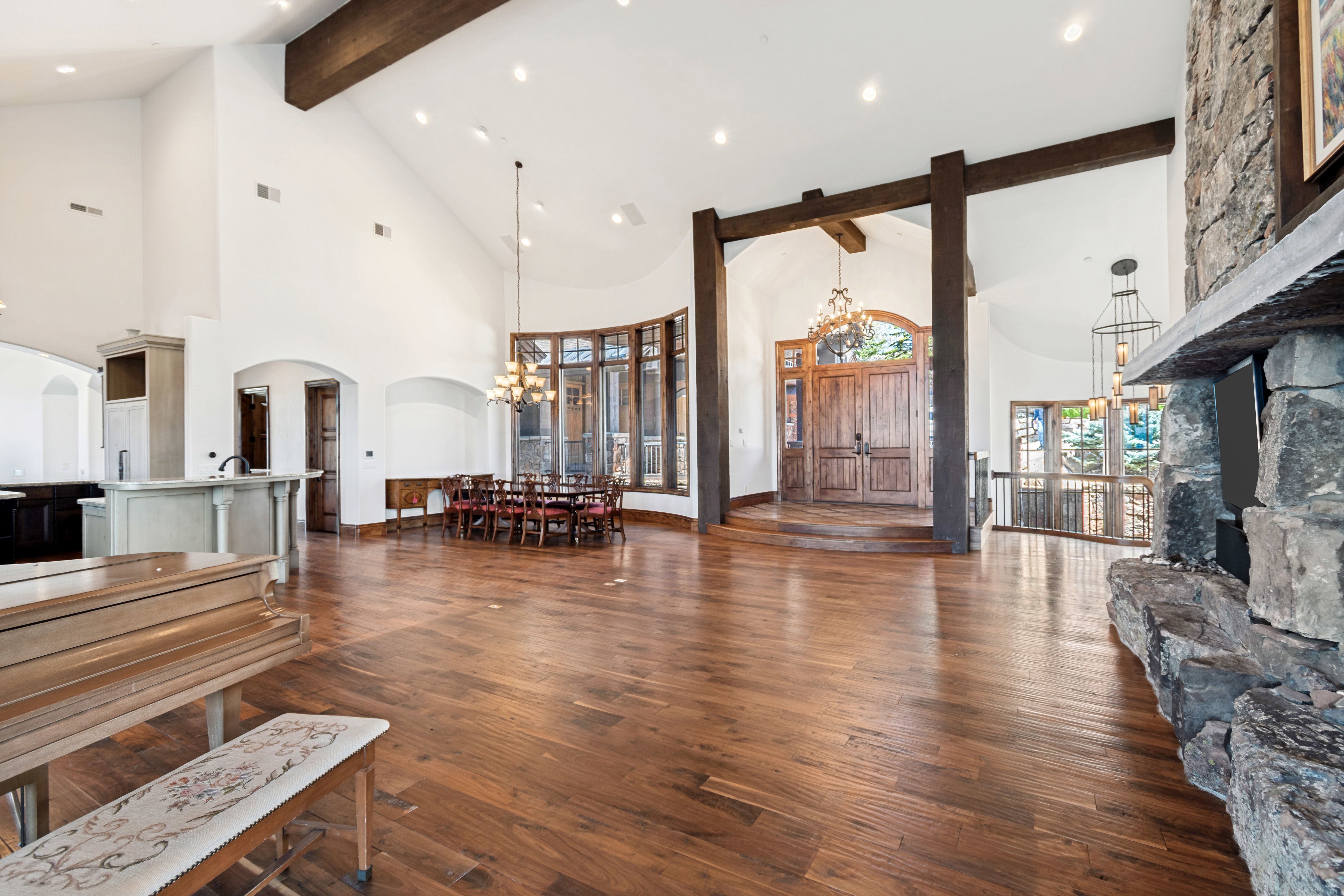 Vaulted great room featuring wood-finish flooring, exposed wood beams, a stone fireplace, and a curved window wall