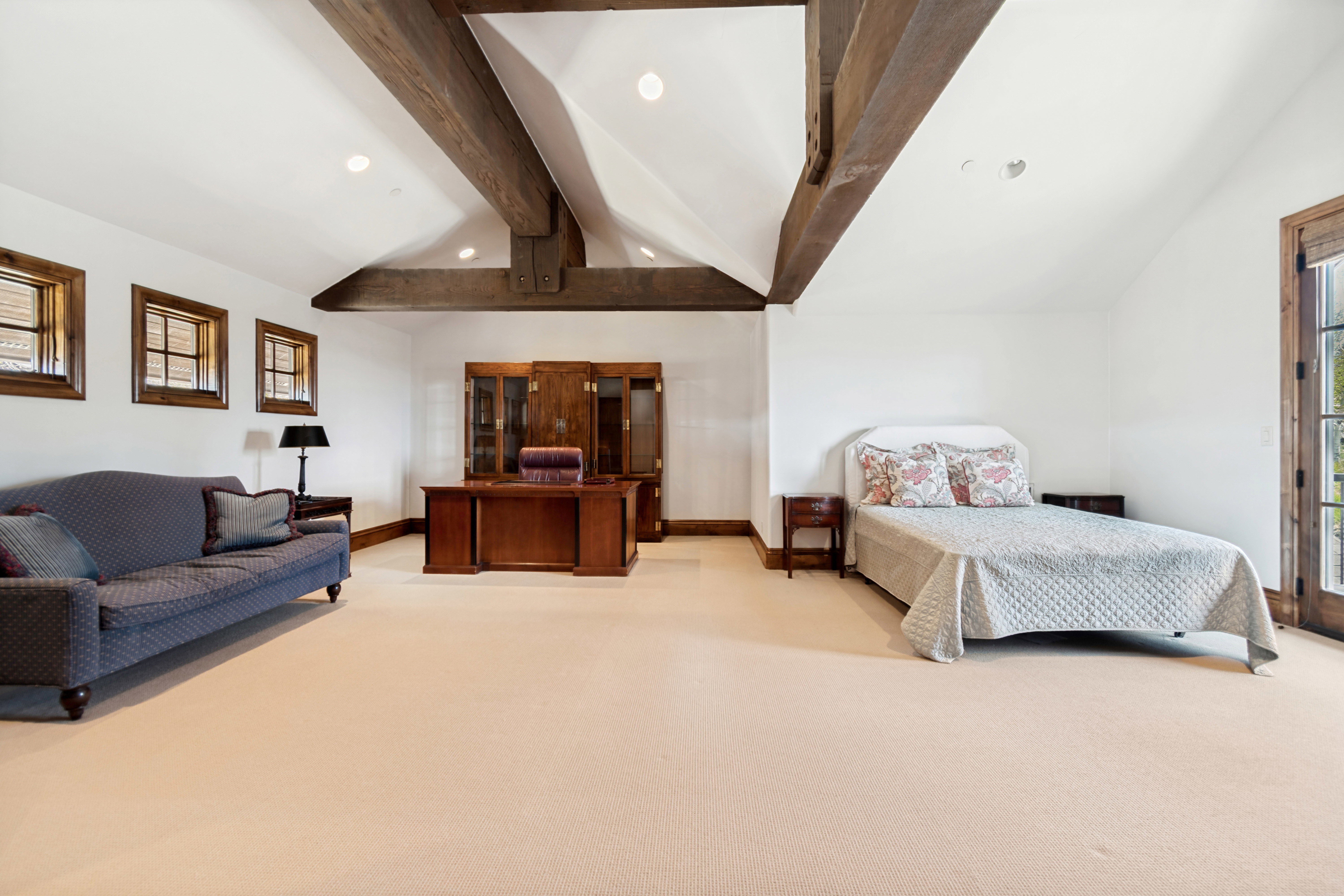Vaulted ceiling with exposed wood beams, recessed lighting, and light-toned carpeting