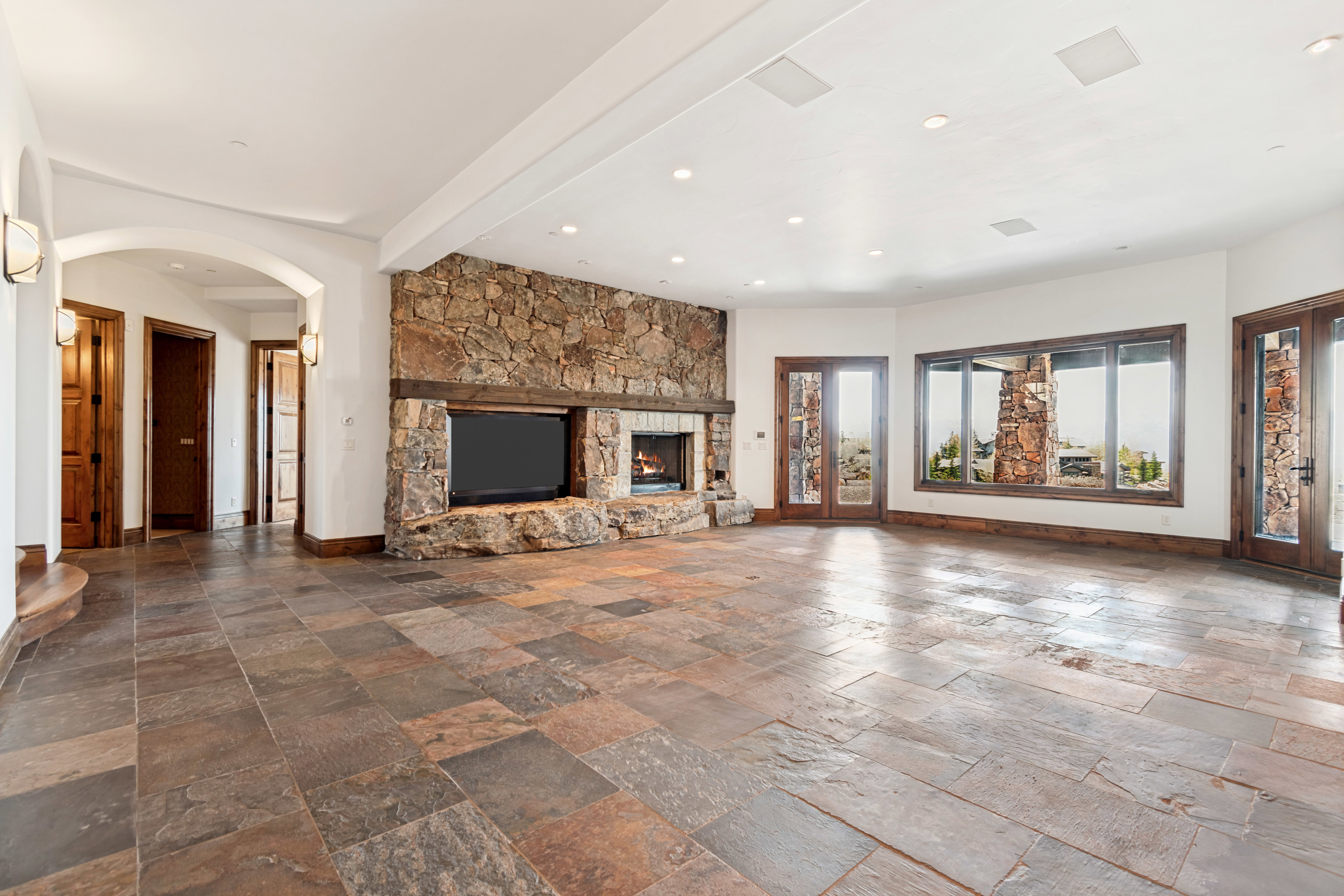Spacious interior featuring natural stone tile flooring, a large stone fireplace with integrated media niche, and multiple wood-framed glass doors