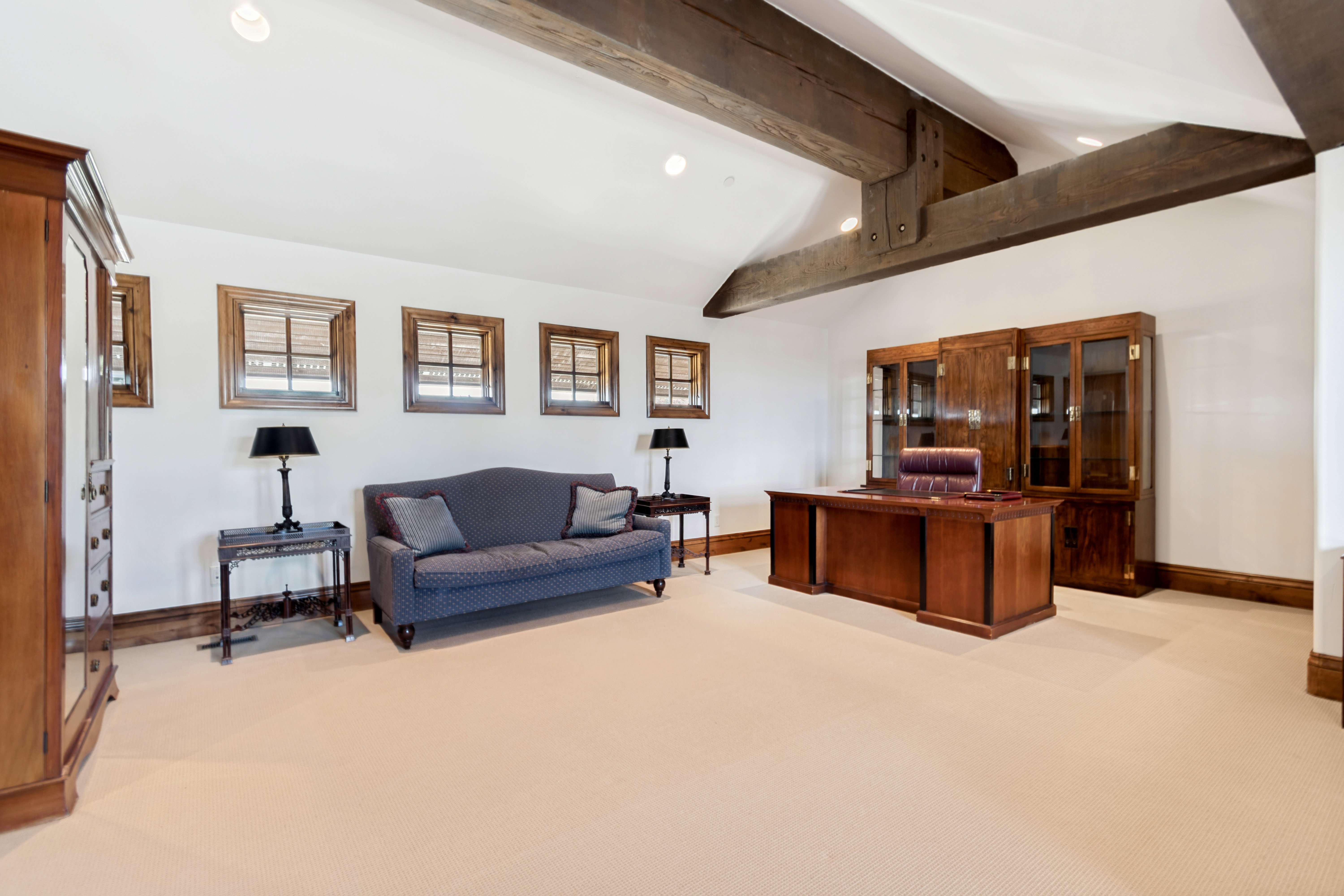Spacious room featuring exposed ceiling beams, multiple windows with wood trim, and cream-toned carpeting