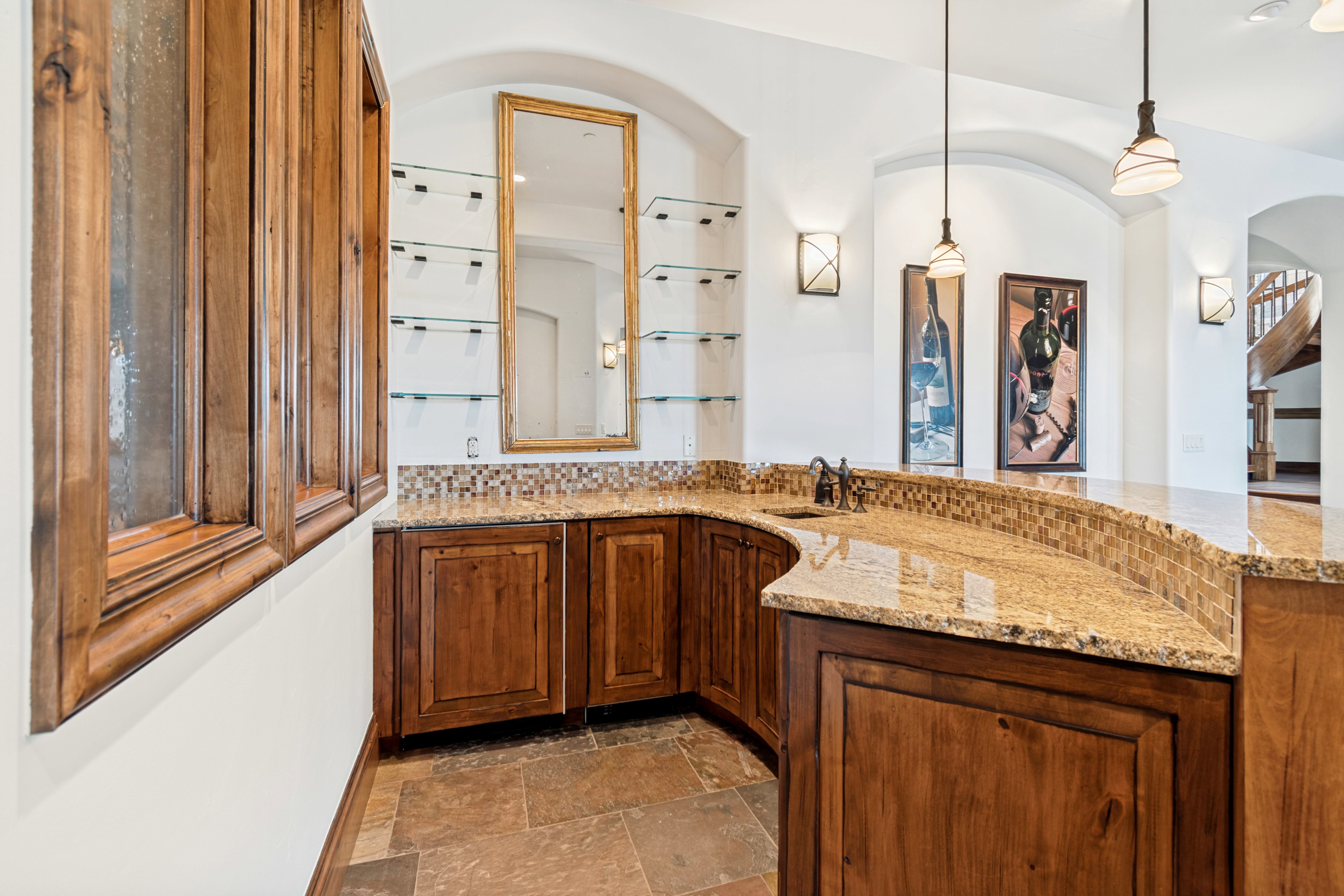 Curved wet bar with granite countertop, integrated sink, and mosaic tile backsplash