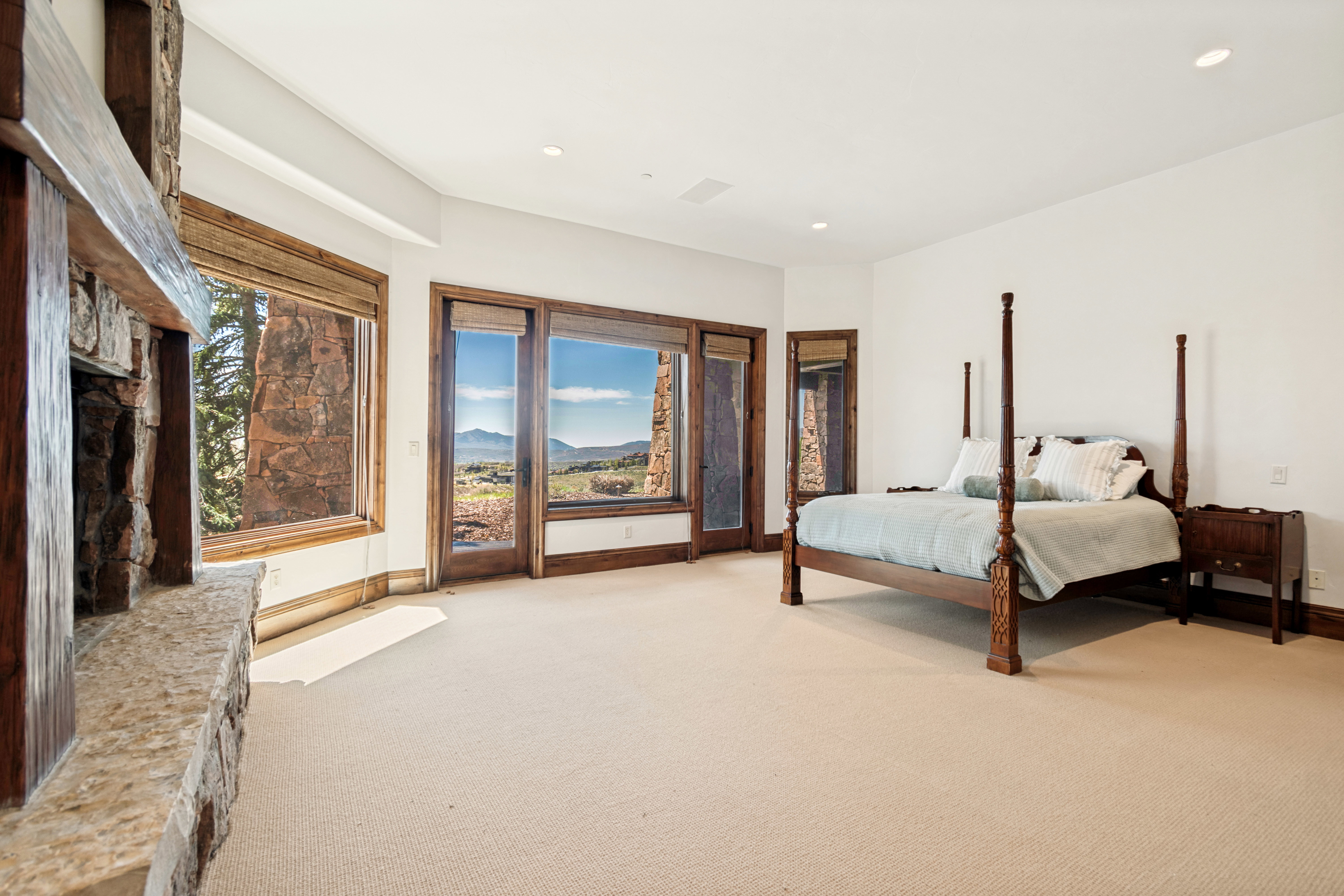 Spacious room with a stone fireplace, wood mantel, and expansive windows