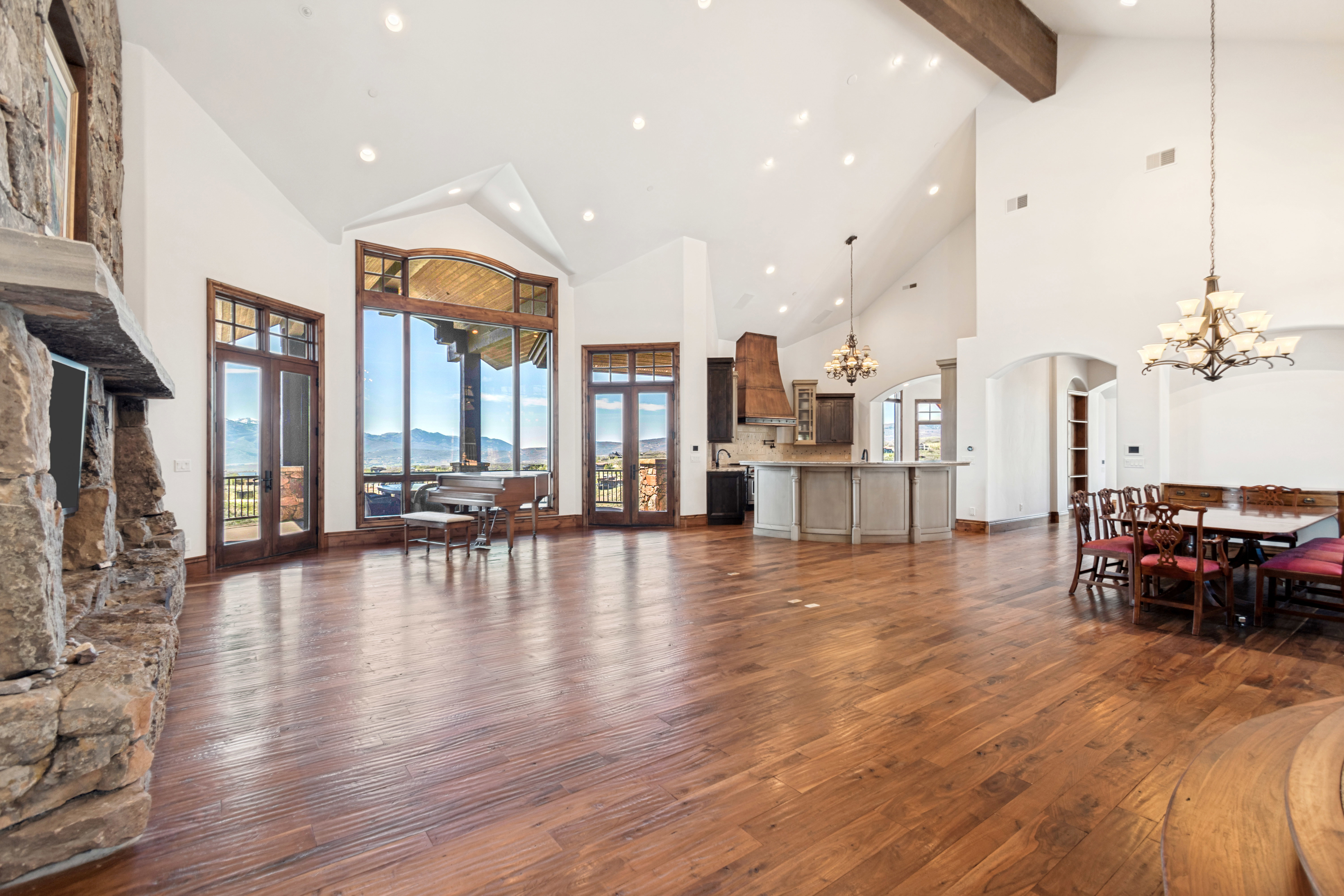 Spacious open-concept living area featuring vaulted ceilings, wood-finish flooring, and a stone-clad fireplace