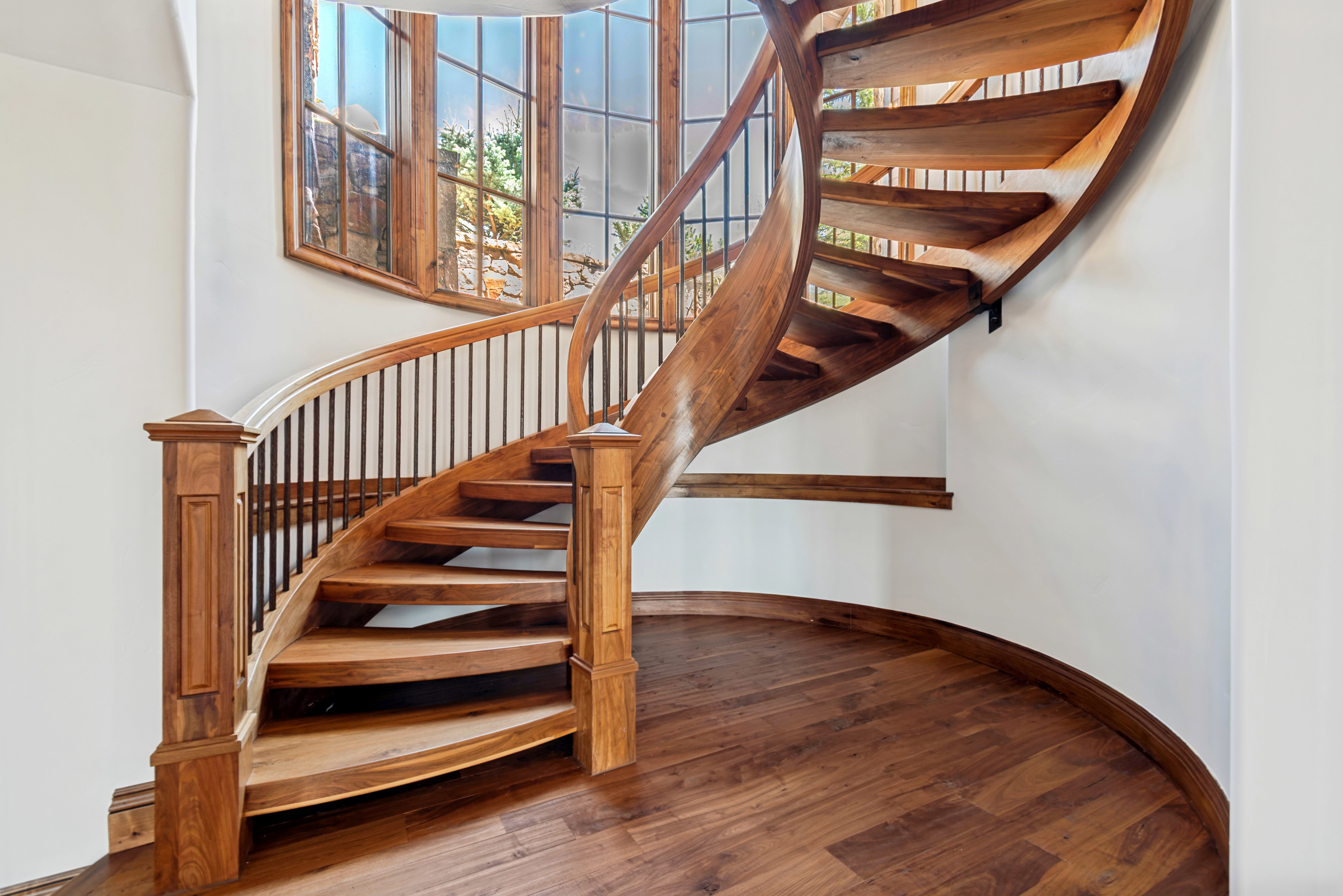 Curved wood staircase featuring wood-finish treads, a matching handrail, and black metal balusters