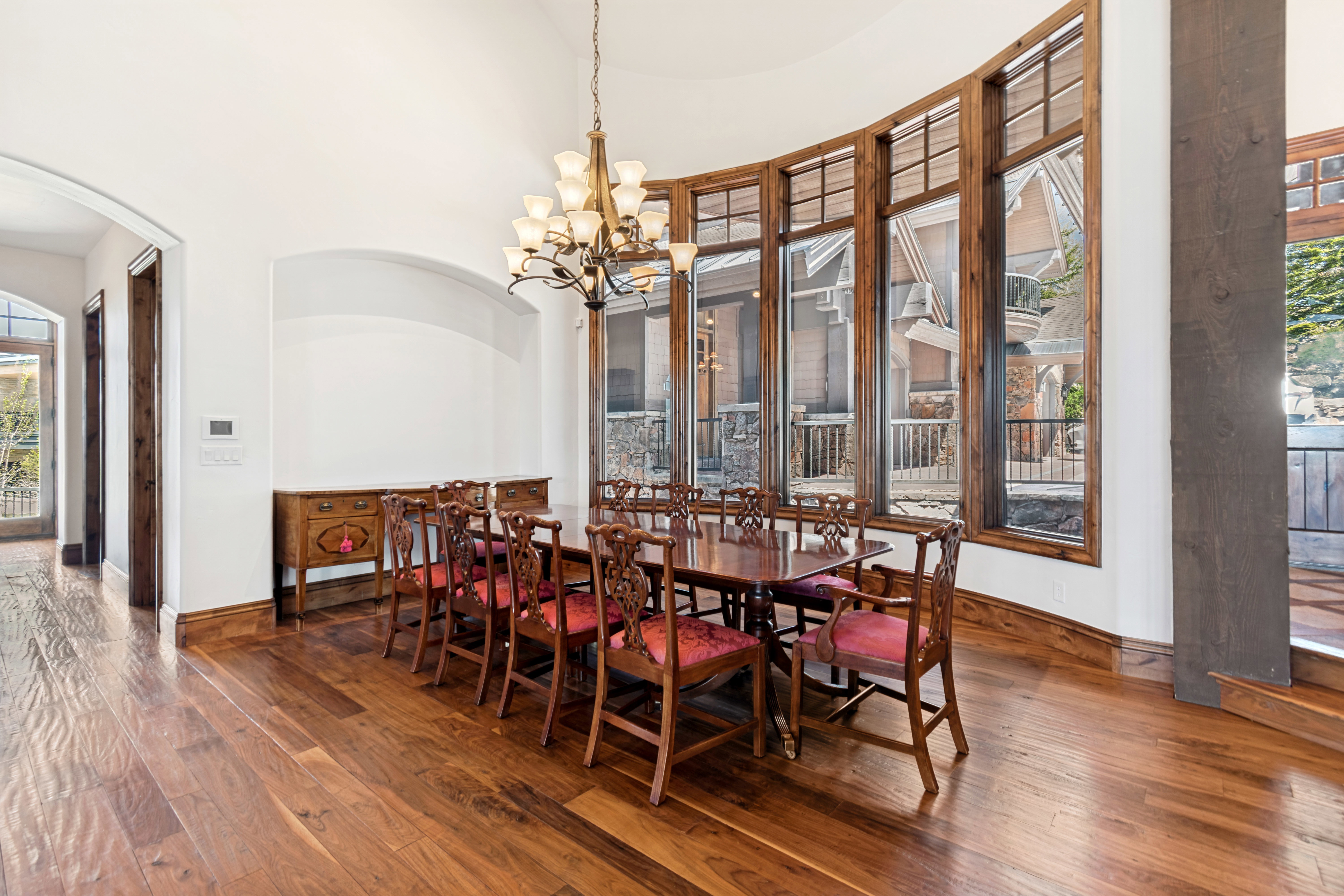 Curved wall of windows with wood frames, wood-finish flooring, arched entryway, built-in wall niche, and an ornate chandelier