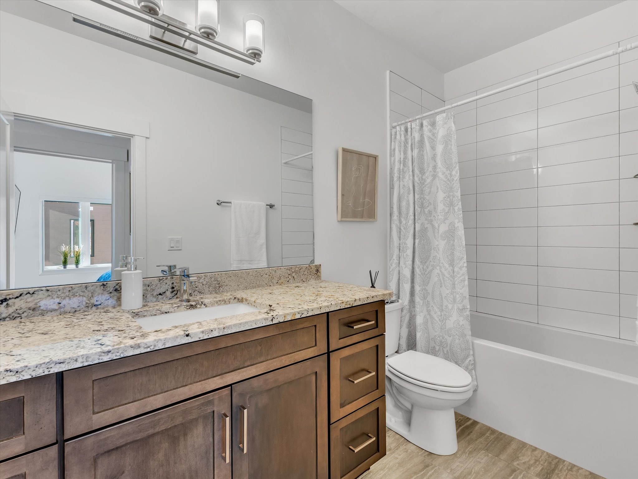 Bathroom featuring a wood-finish vanity with granite-style countertop, integrated rectangular sink, and chrome fixtures