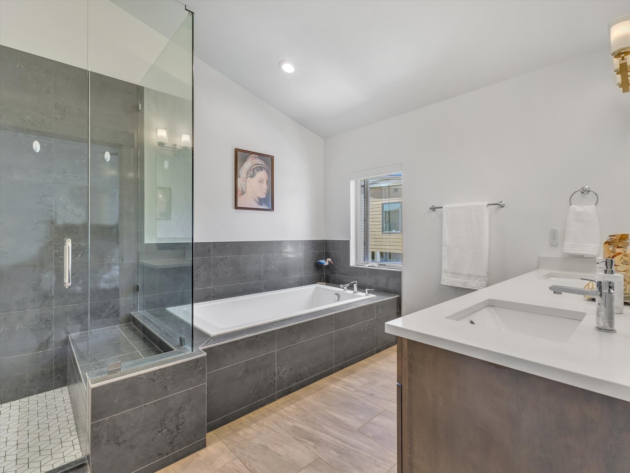 Spacious bathroom featuring a glass-enclosed shower with a built-in bench, a separate soaking tub, and a dual-sink vanity with white countertops
