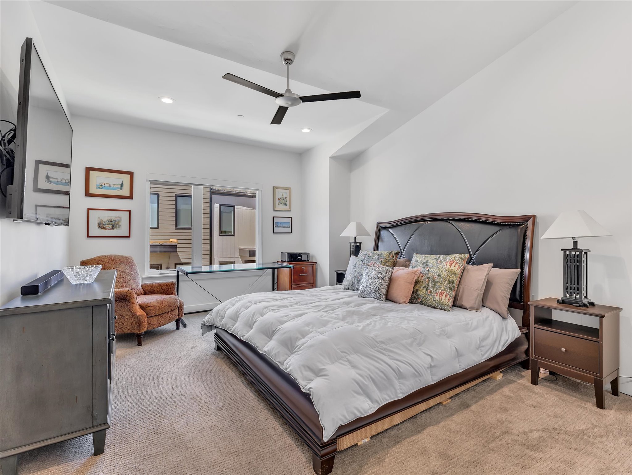 Carpeted room featuring a ceiling fan with recessed lighting, a dark wood-finish bed frame with an upholstered headboard, and sliding glass doors