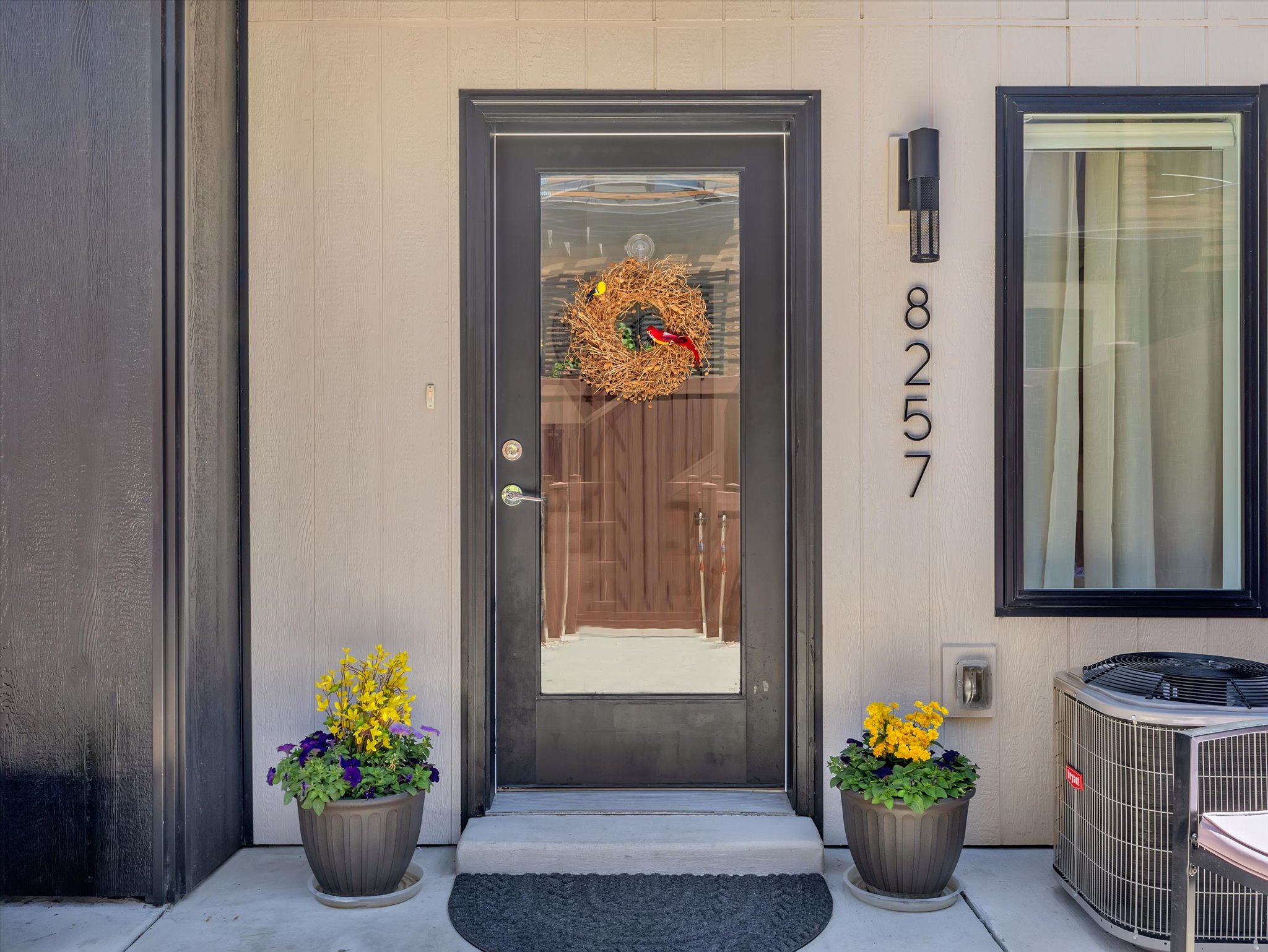 Vertical siding exterior featuring a black frame glass entry door, modern wall sconce, and contemporary house numbers