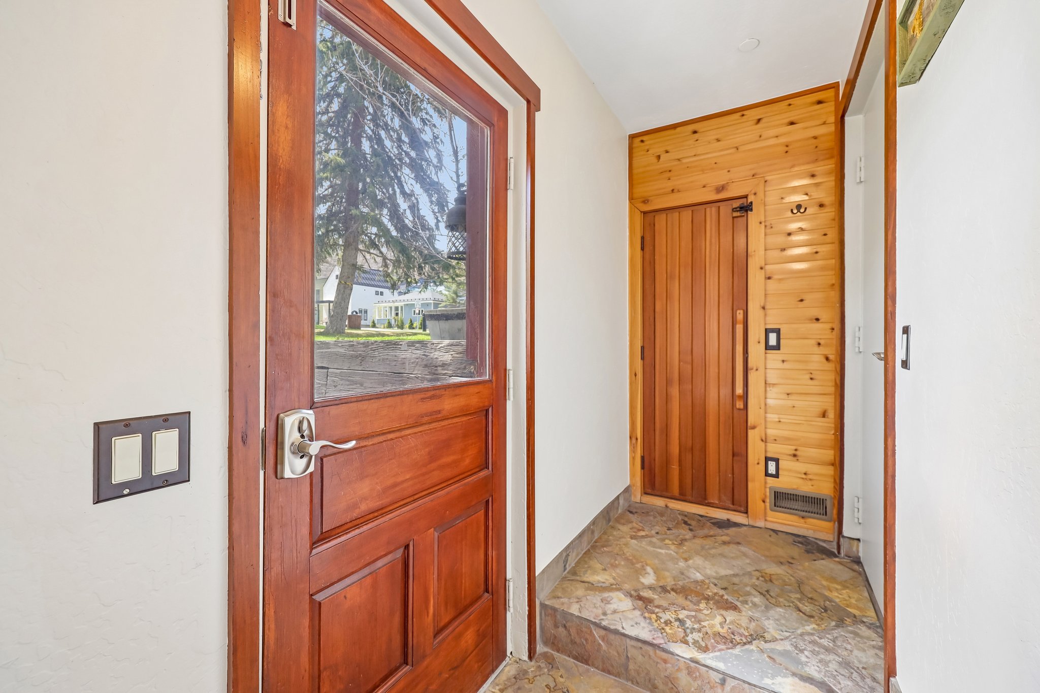 Entryway featuring a wood-panel accent wall, natural stone flooring, and a solid wood door with an inset glass panel