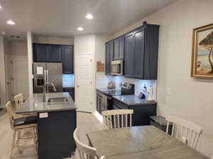 Modern kitchen featuring navy cabinetry, stainless steel appliances, a subway tile backsplash, and a central island with an undermount sink and bar seating