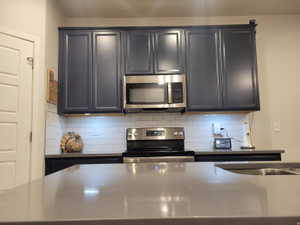 Contemporary kitchen featuring rich blue cabinetry, stainless steel appliances, subway tile backsplash, under-cabinet lighting, and a large countertop with an integrated sink