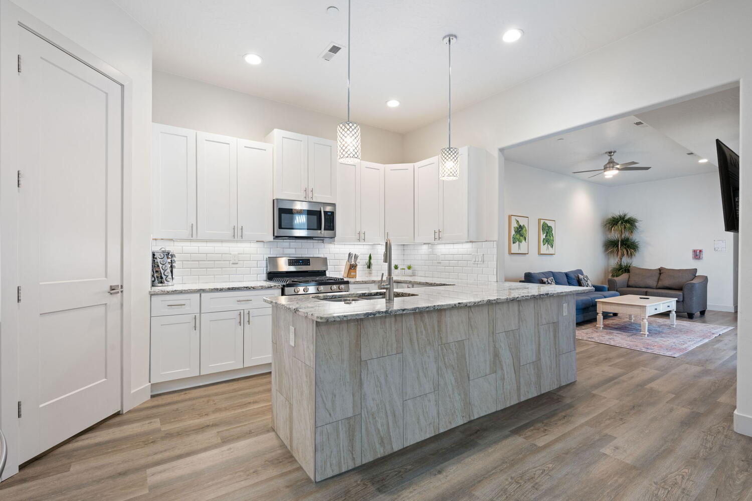 Modern kitchen featuring a large island with a sink, stainless steel appliances, white cabinetry, a subway tile backsplash, and light wood-finish flooring