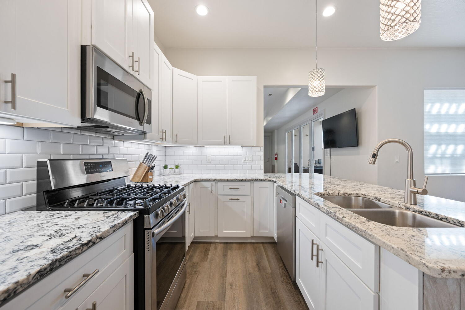 Modern kitchen featuring white cabinetry, granite countertops, subway tile backsplash, stainless steel appliances, and wood-finish flooring