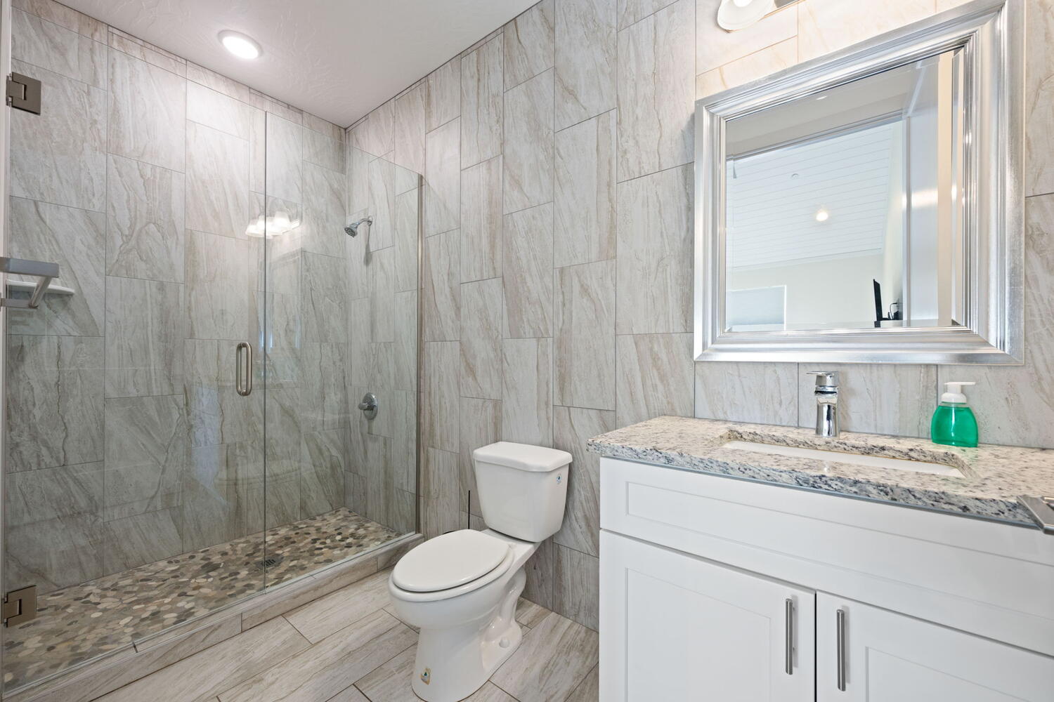 Glass-enclosed shower with pebble flooring and tiled walls